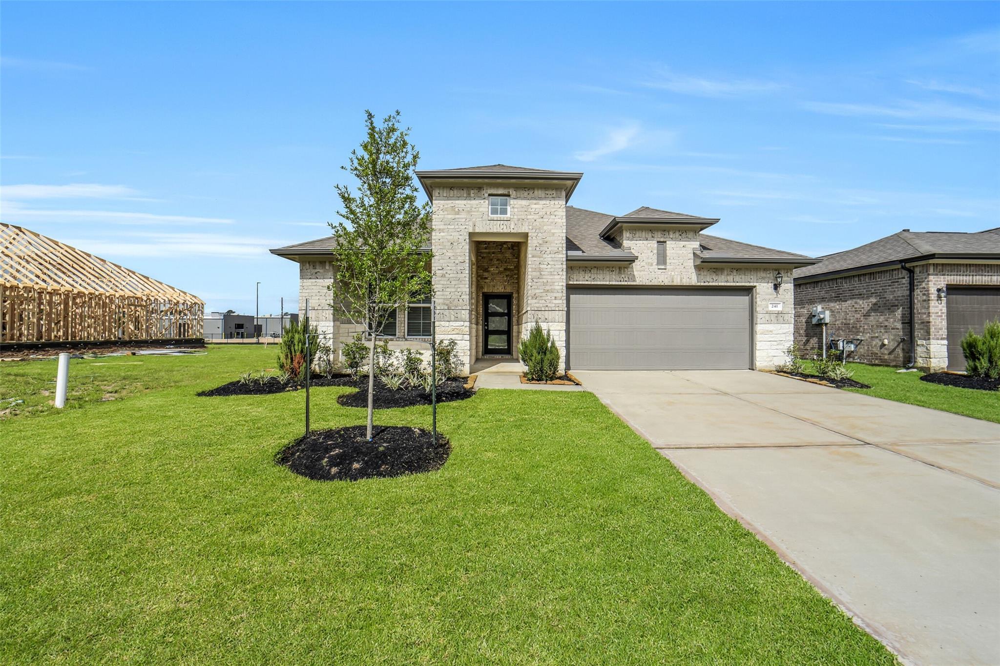 Modern brick and stone 4-bedroom home with 2-car garage, landscaped yard, and driveway in Windmill Estates, Magnolia, Texas
