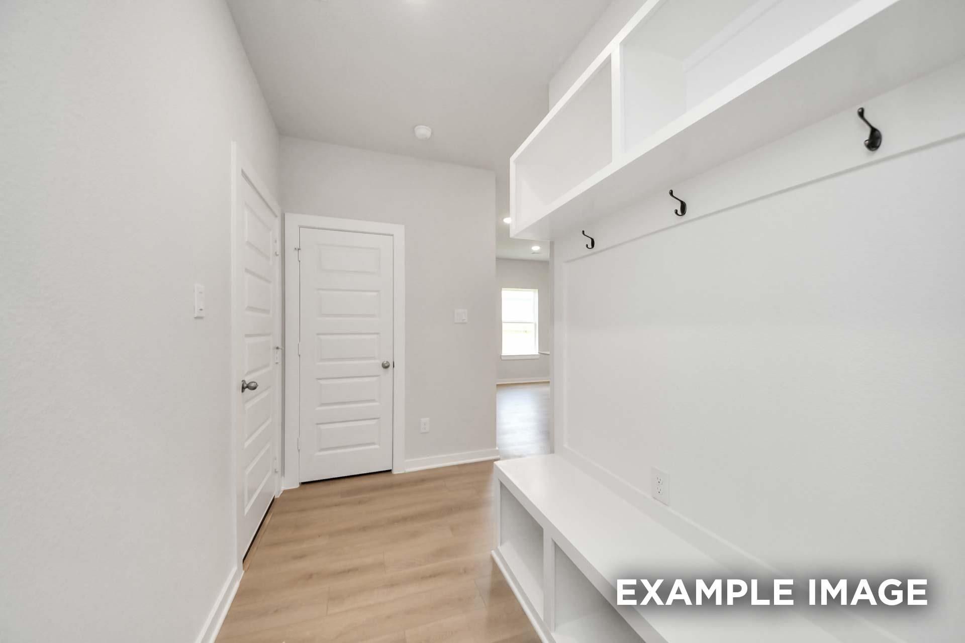 White mudroom with built-in bench, coat hooks, and storage cubbies in Davidson Homes The Blanco E, Windmill Estates, Magnolia, TX