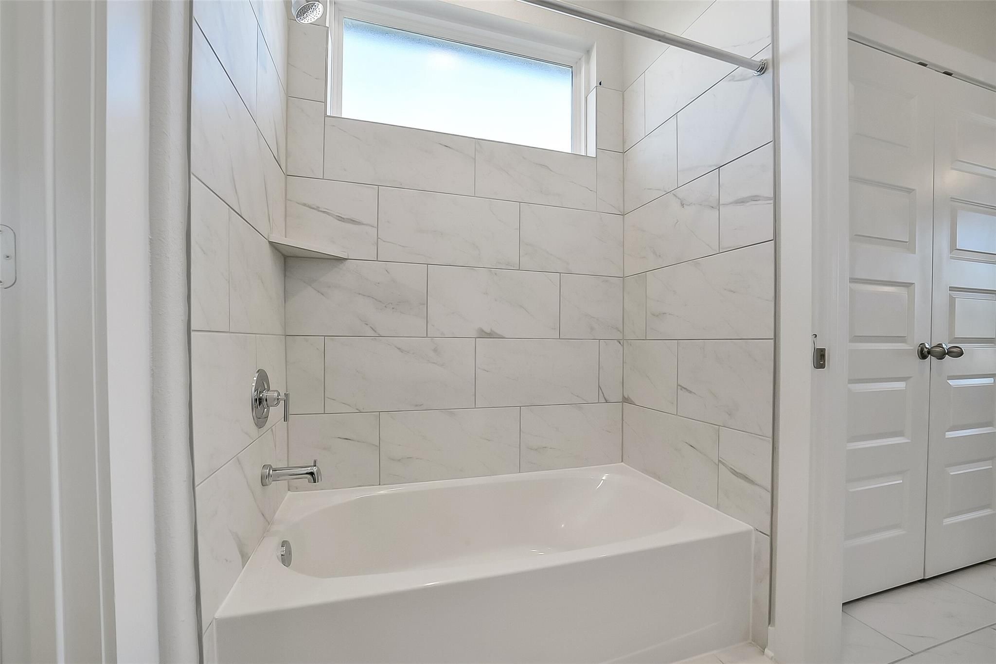 Elegant master bathroom with white subway tile, soaking tub-shower combo, and frosted window in Davidson Homes The Acadia A, Sunterra, Katy, Texas