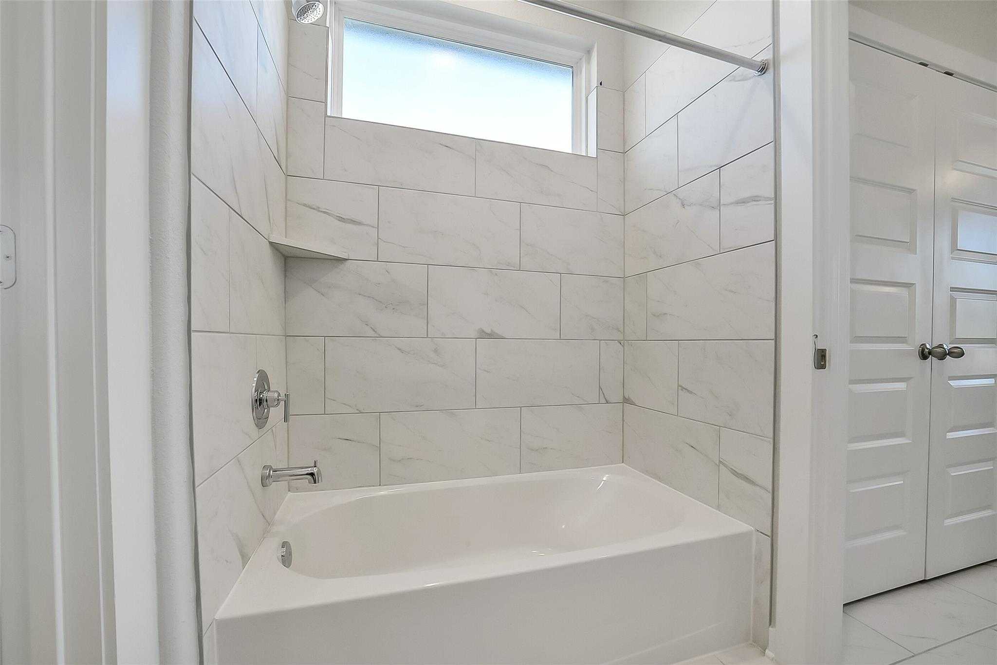Elegant master bathroom with white subway tile, soaking tub-shower combo, and frosted window in Davidson Homes The Acadia A, Sunterra, Katy, Texas