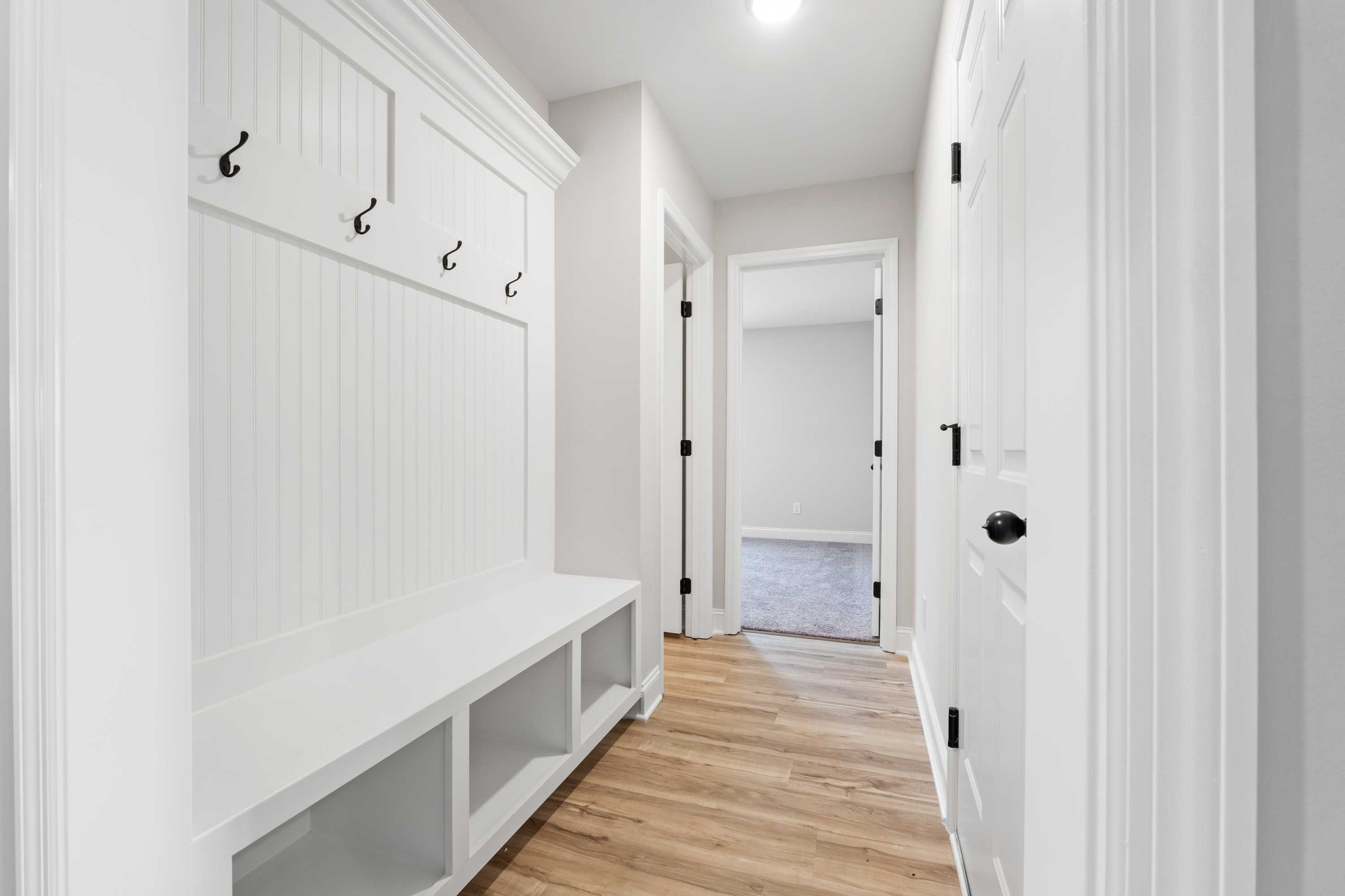 Spacious mudroom in The Everett with white built-in lockers, coat hooks, storage bench, and hardwood floors