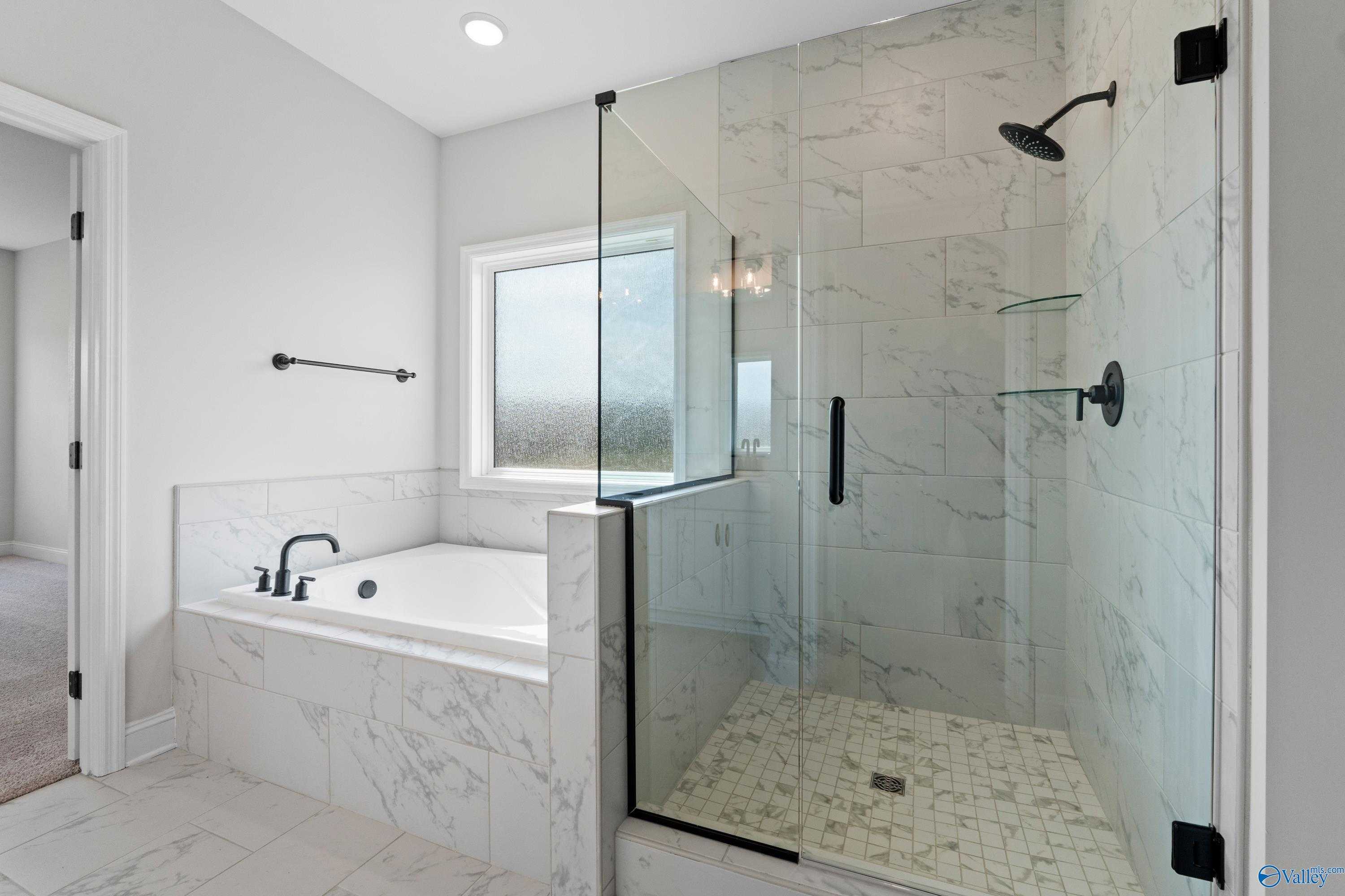 Modern master bathroom with frameless glass shower, marble tiles, and soaking tub in Davidson Homes The Rockford, Toney, Alabama