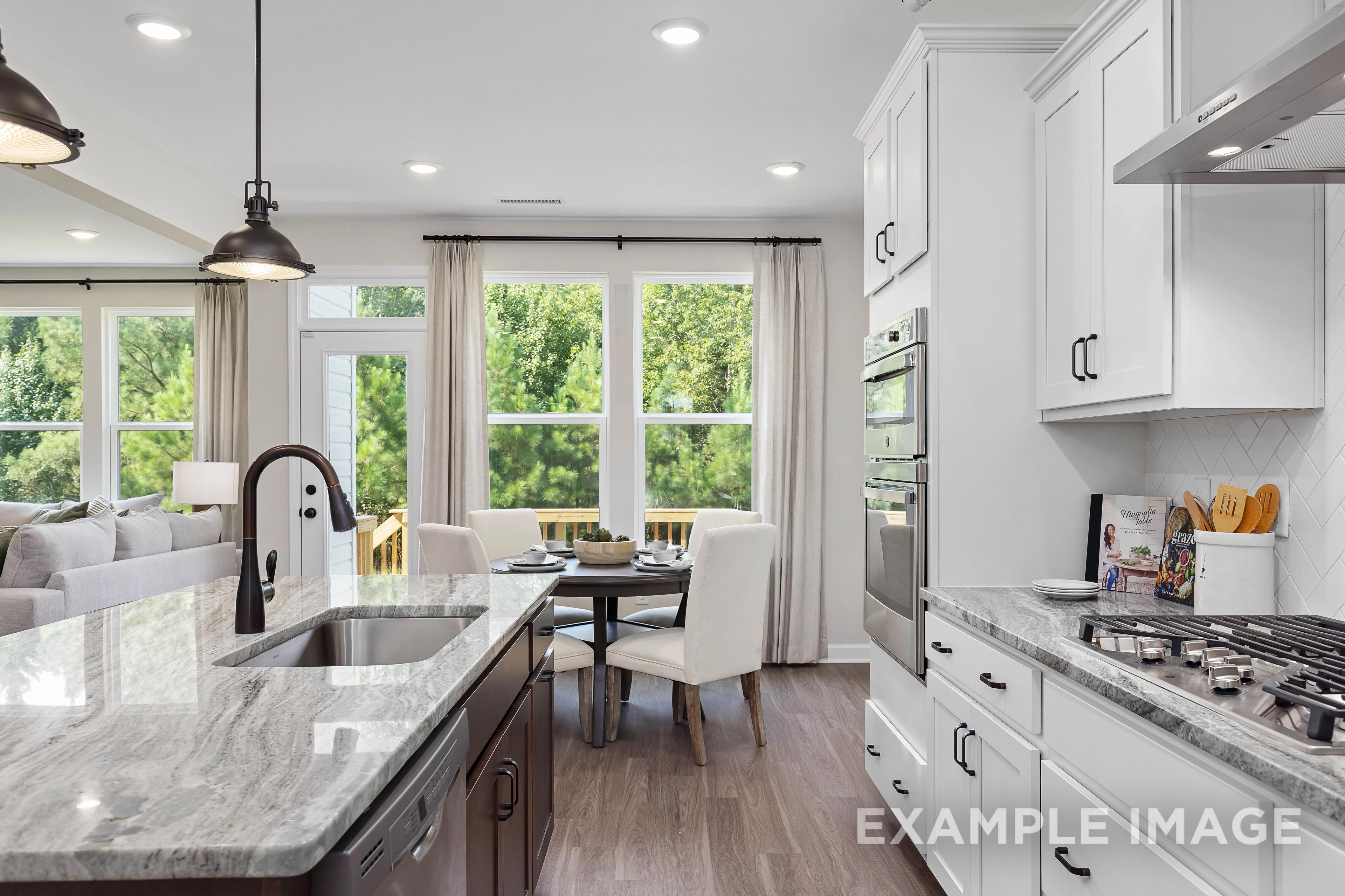 Spacious open-concept kitchen in The Willow B with white shaker cabinets, quartz counters, gas range, and sunny dining nook