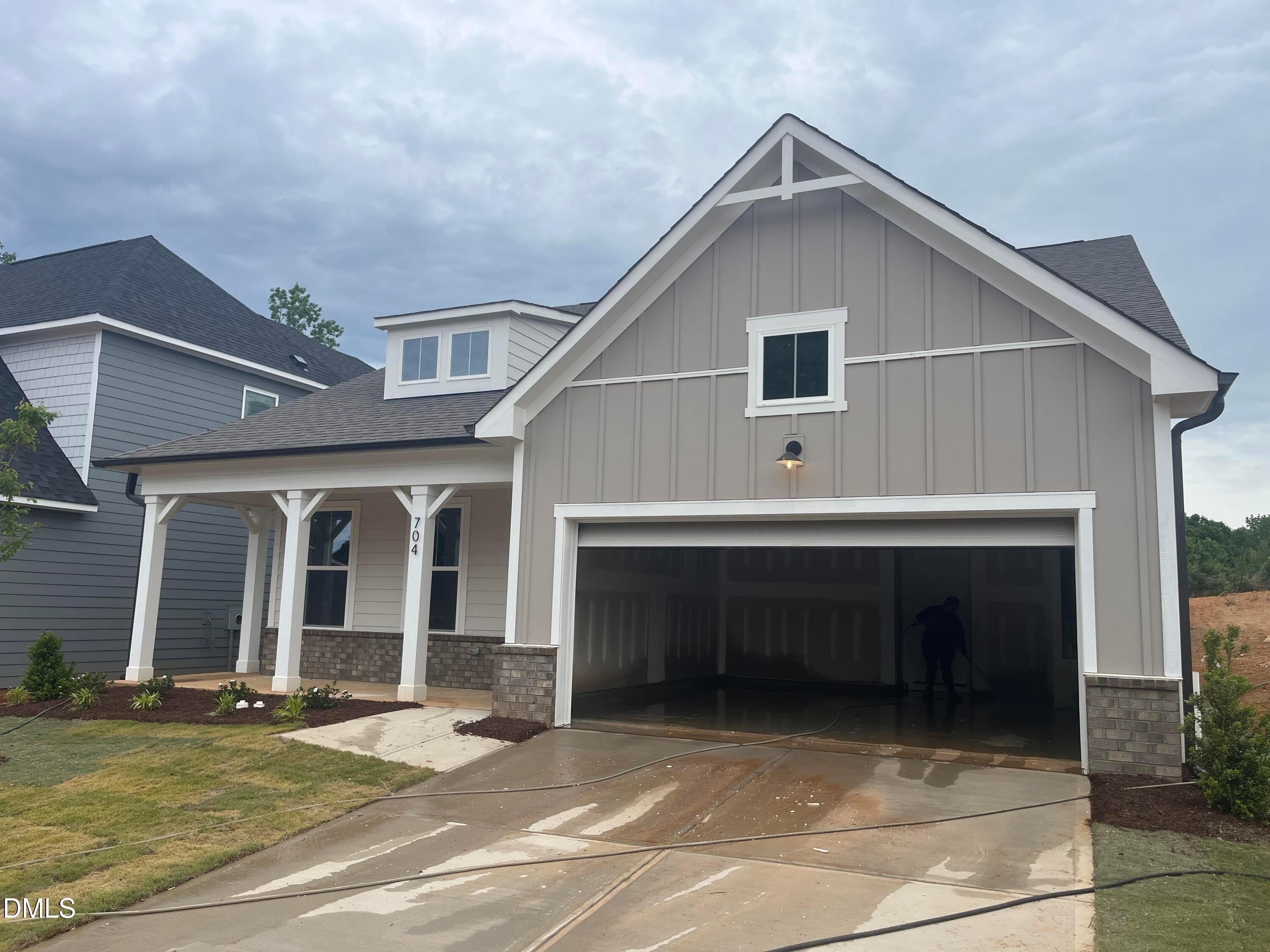 Gray two-story craftsman home with open 2-car garage, columned front porch, brick accents, and landscaping in Wake Forest, NC