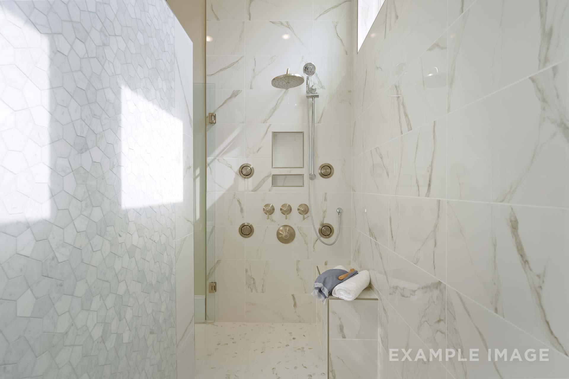 Spacious walk-in shower in The Seaside C master bathroom with white marble tiles, multiple rain showerheads, and built-in bench