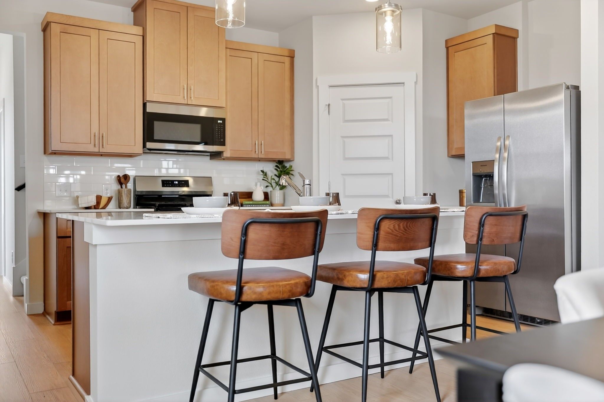 Modern kitchen with light wood cabinets, quartz island, and bar seating in The Sabine J floor plan by Davidson Homes, Heartland.
