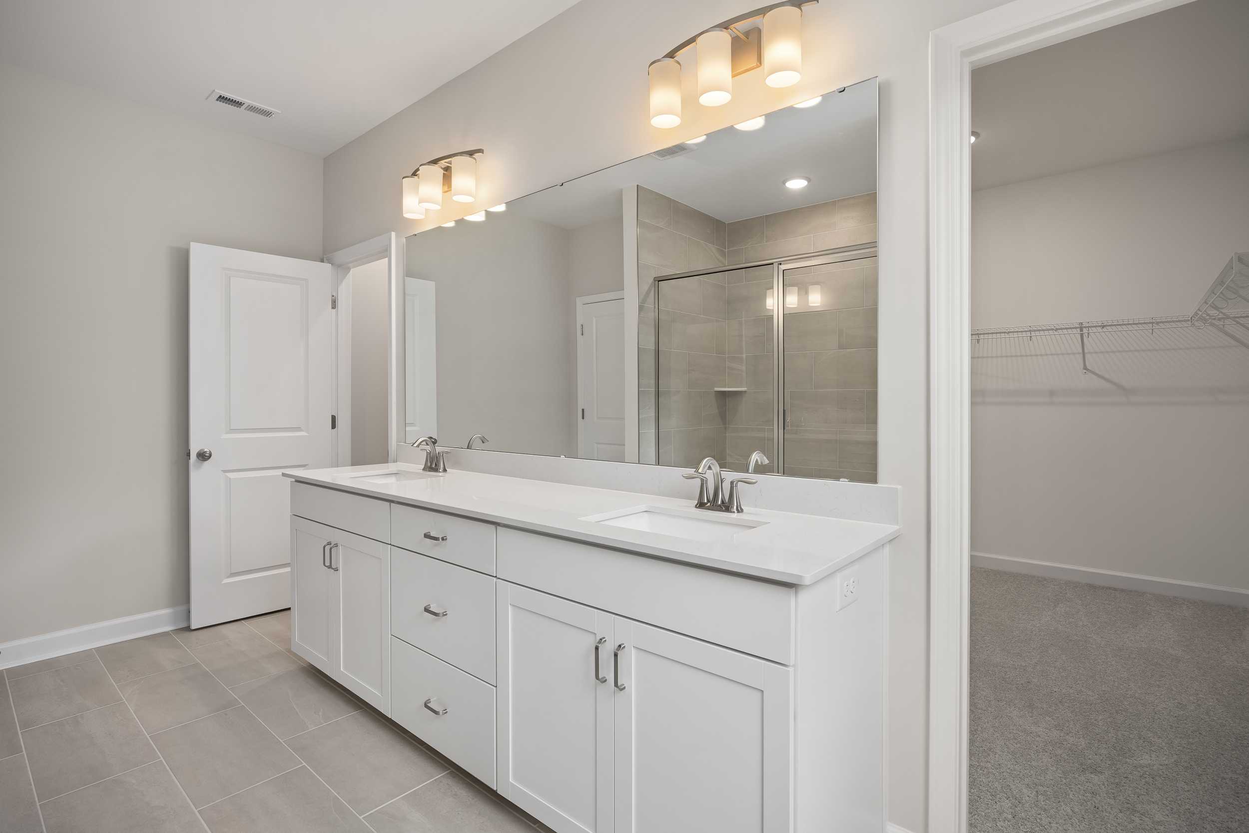 Spacious master bathroom in The Beech C with double white vanity, large mirrors, and frameless walk-in shower