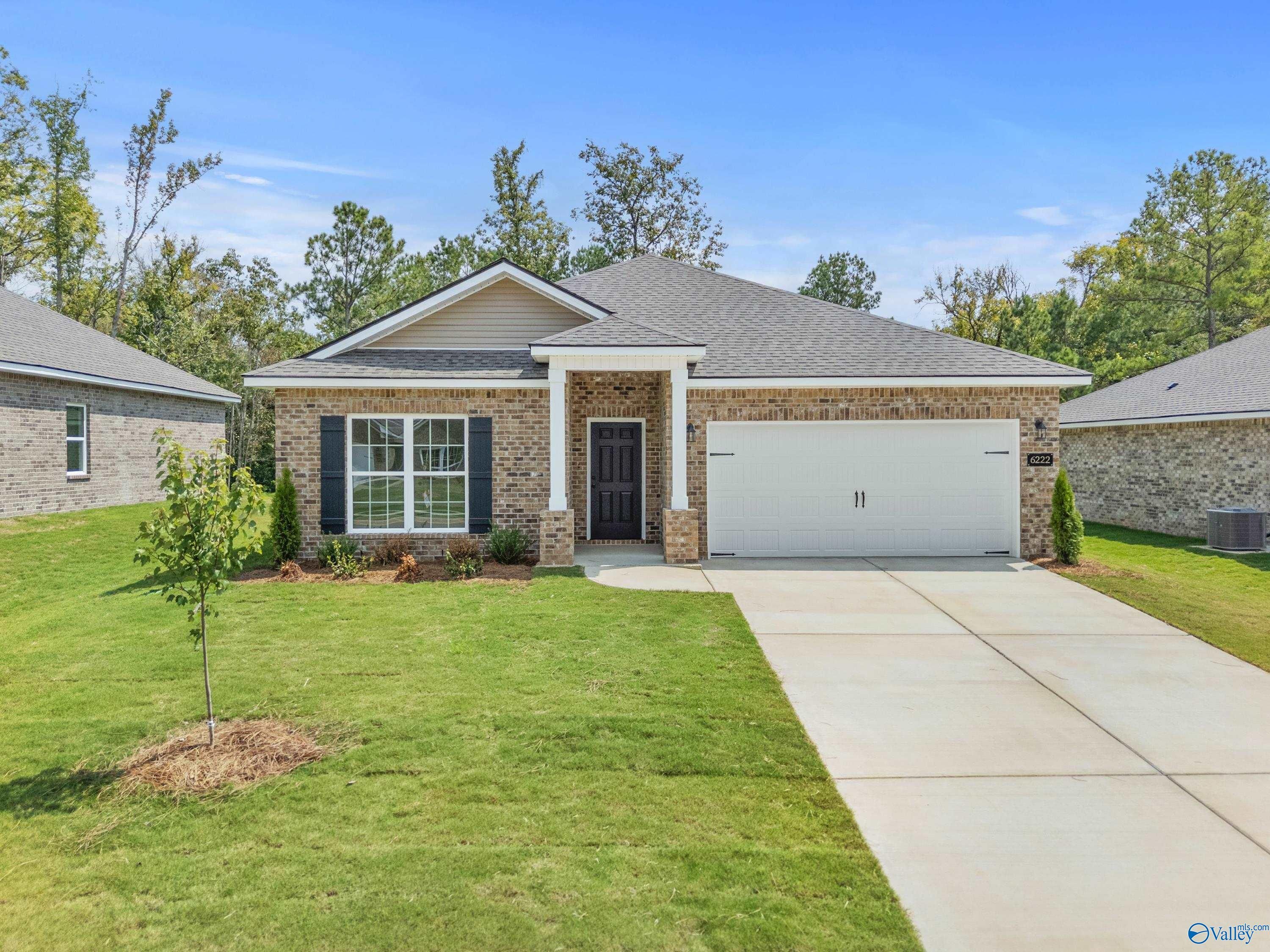 Single-story beige brick home with 2-car garage, covered porch, and lush front yard in Spragins Cove, Huntsville, Alabama