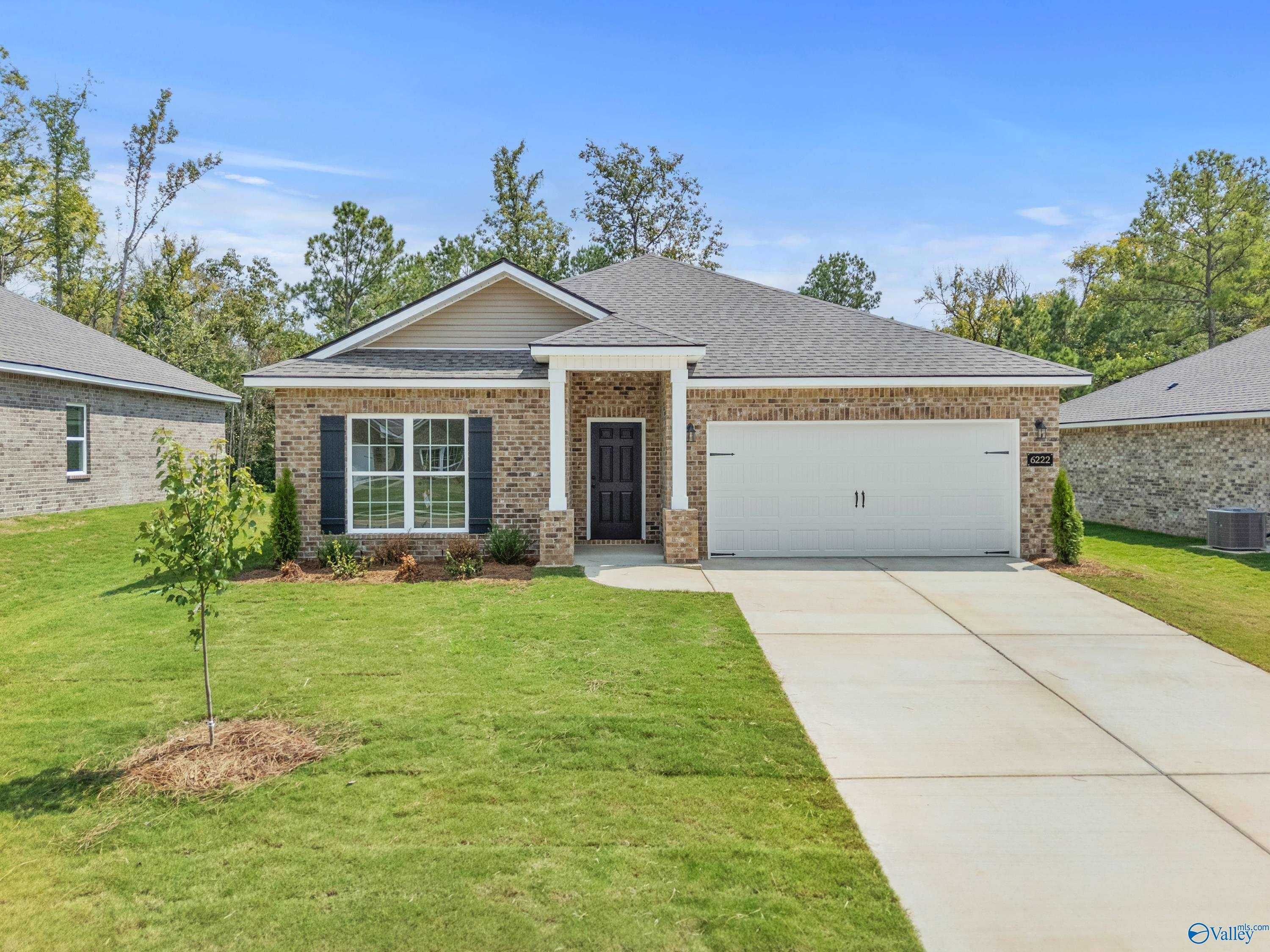 Single-story beige brick home with 2-car garage, covered porch, and lush front yard in Spragins Cove, Huntsville, Alabama