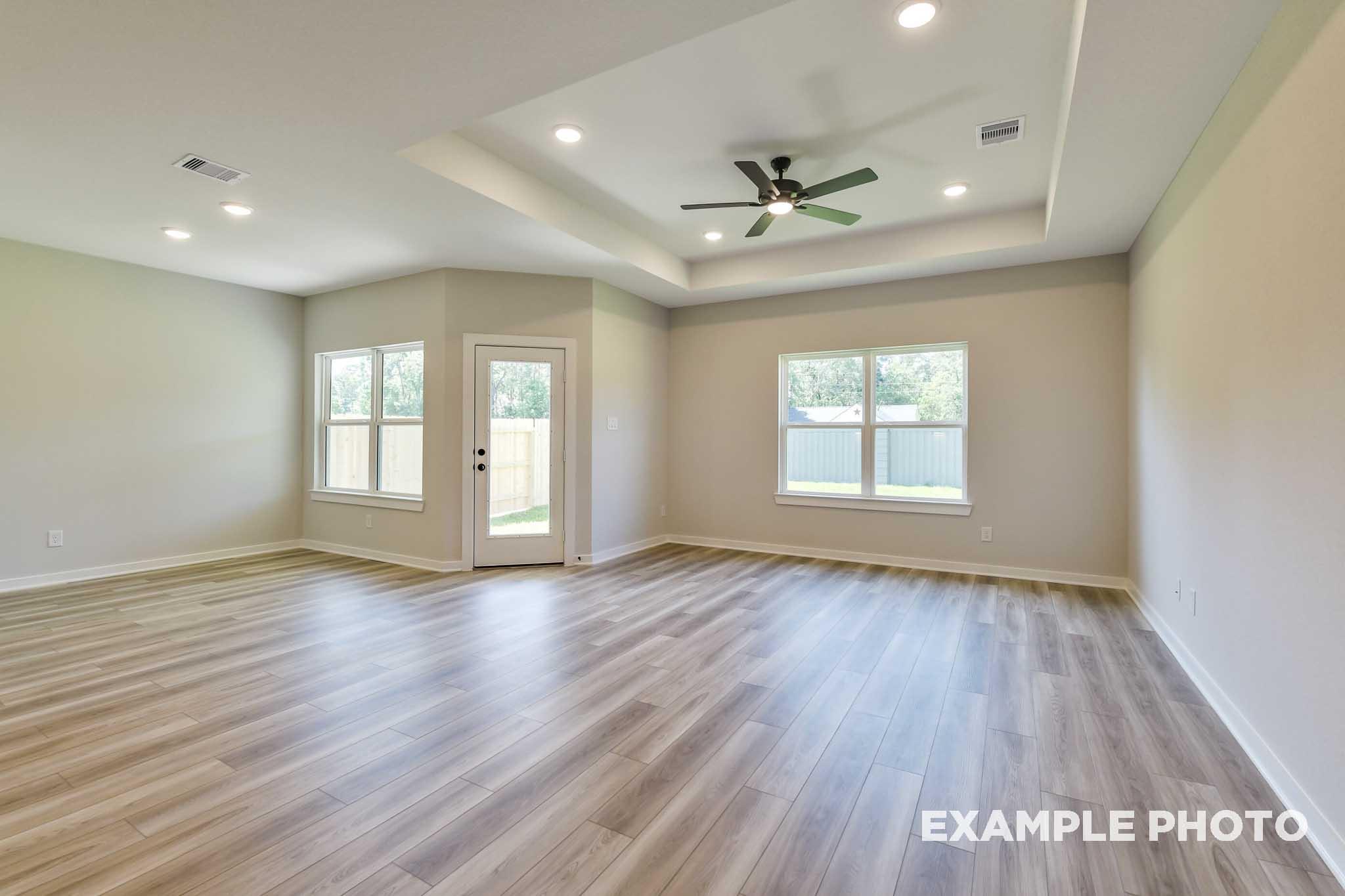 Spacious open living room in The Daphne G home with light wood floors, tray ceiling, ceiling fan, and large windows