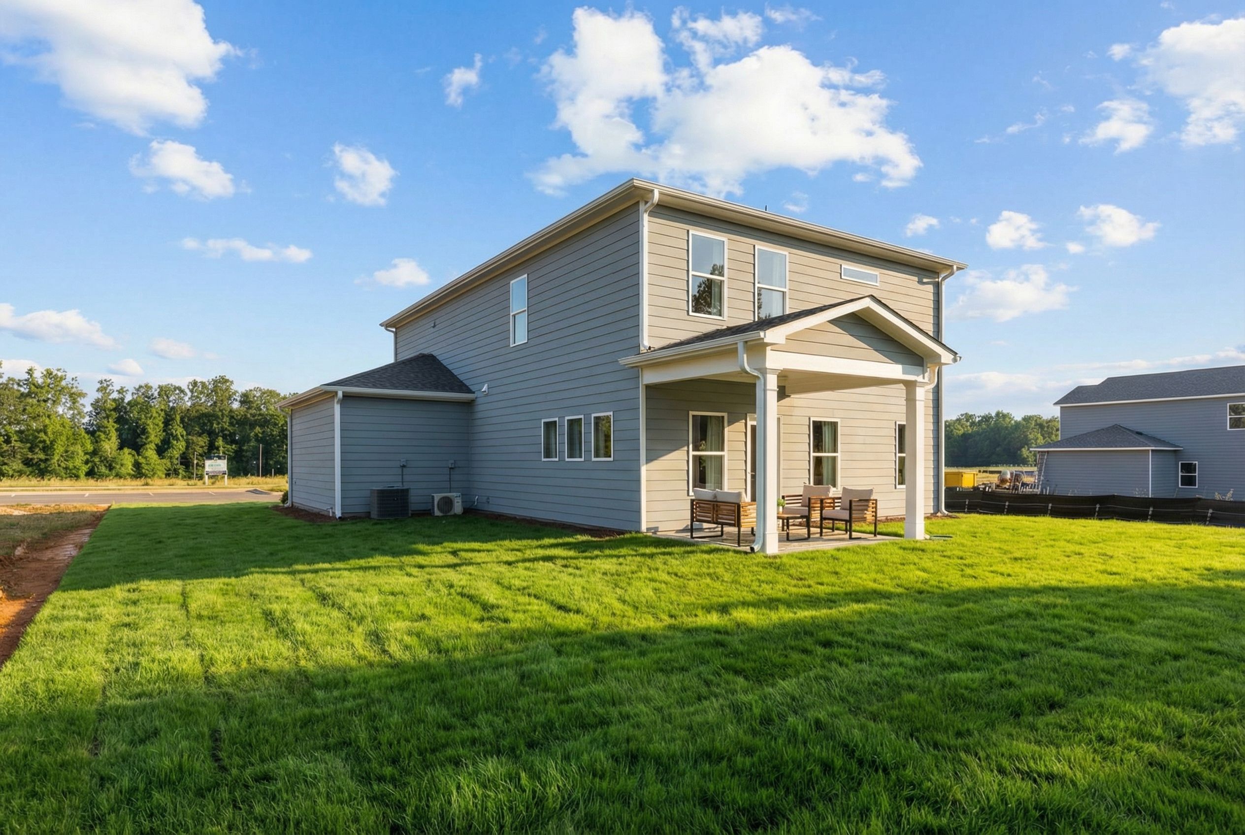 Two-story gray siding home at Cedar Farms in Winder, Georgia with covered porch, patio seating, and lush green lawn