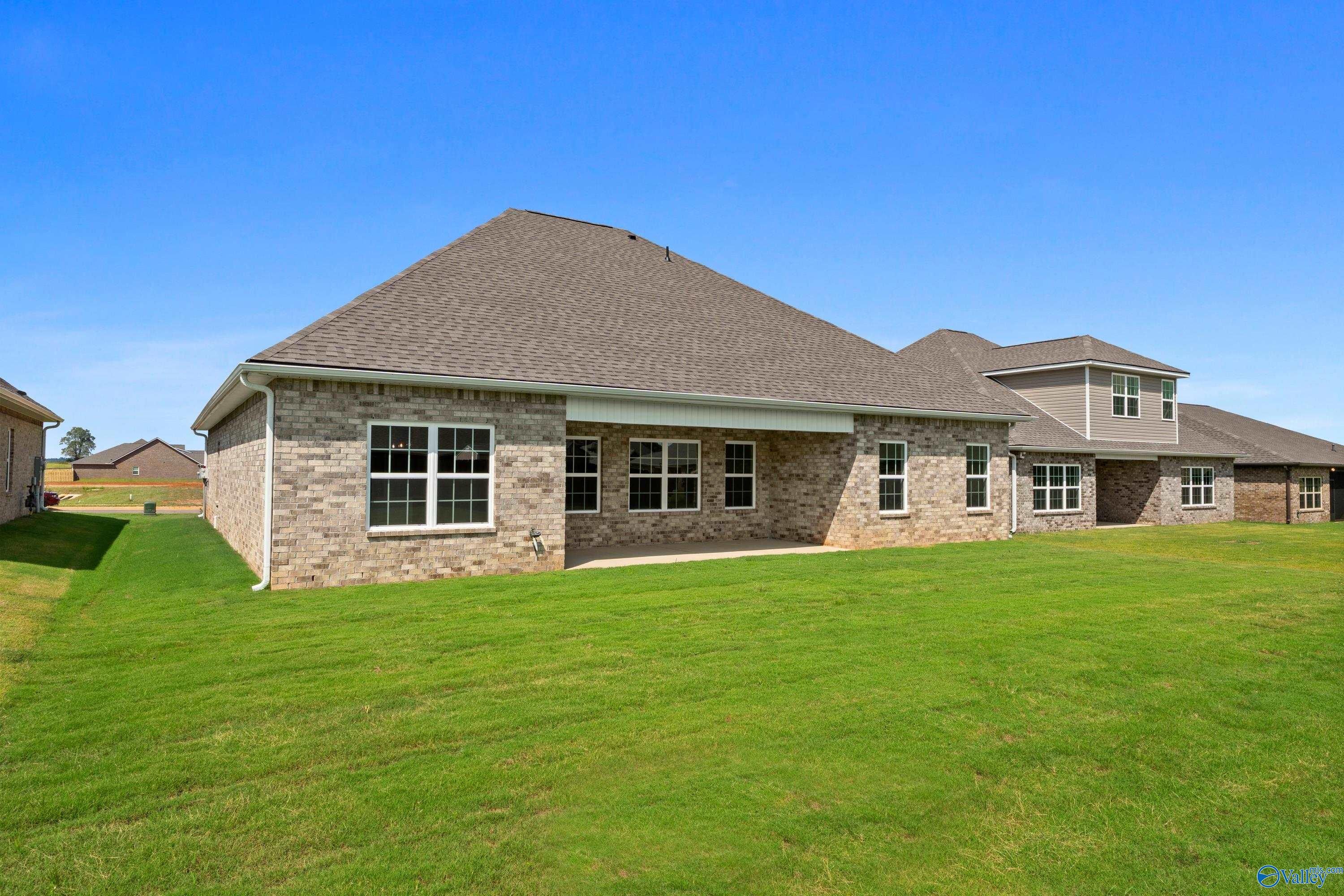 Brick exterior of 1.5-story The Rockford B home with covered patio, lush green lawn, and blue sky in Kendall Downs, Toney, Alabama