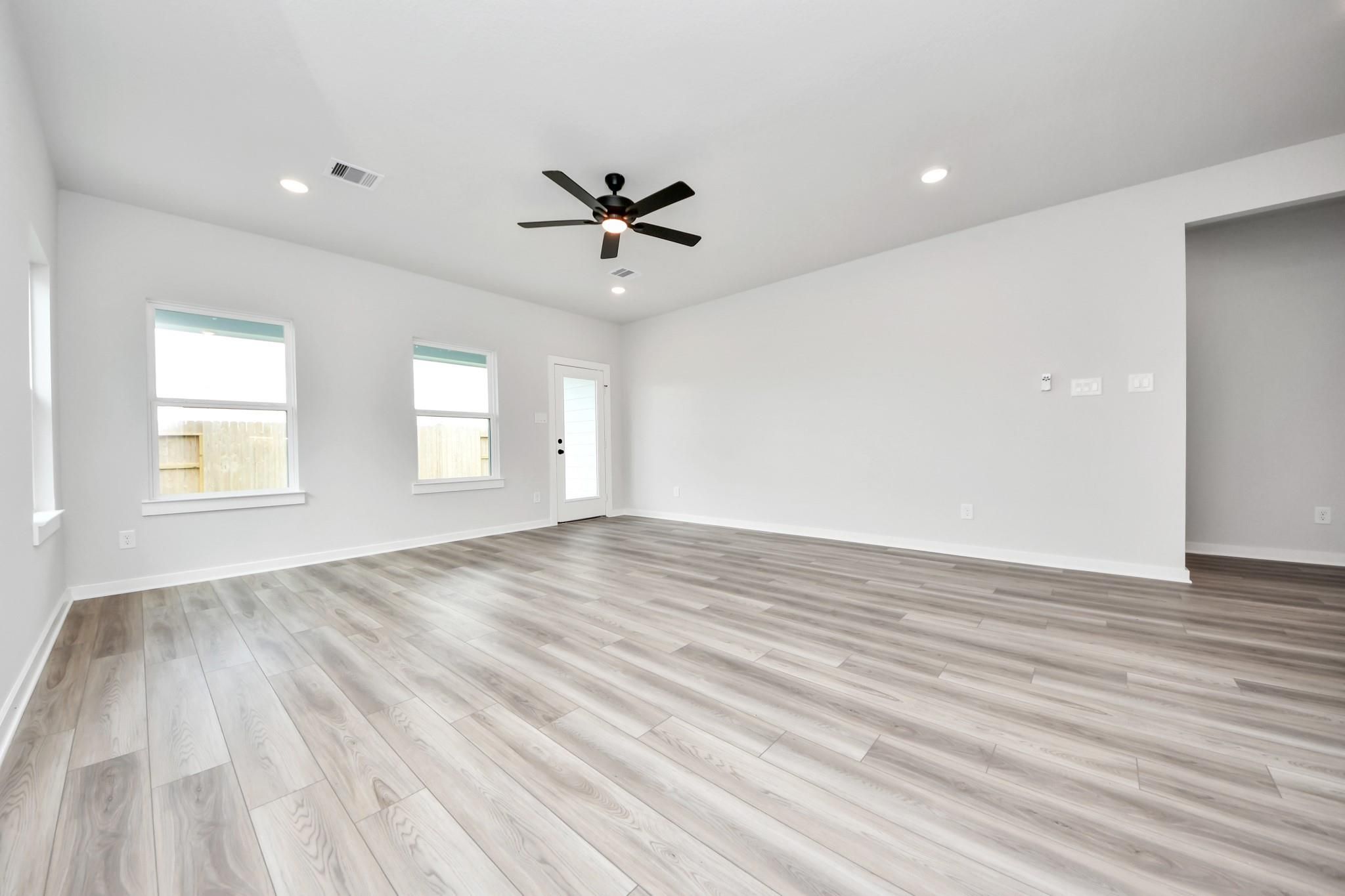 Spacious, light-filled living room with wood-look flooring in The Sorrento E floor plan by Davidson Homes in Crosby, Texas.
