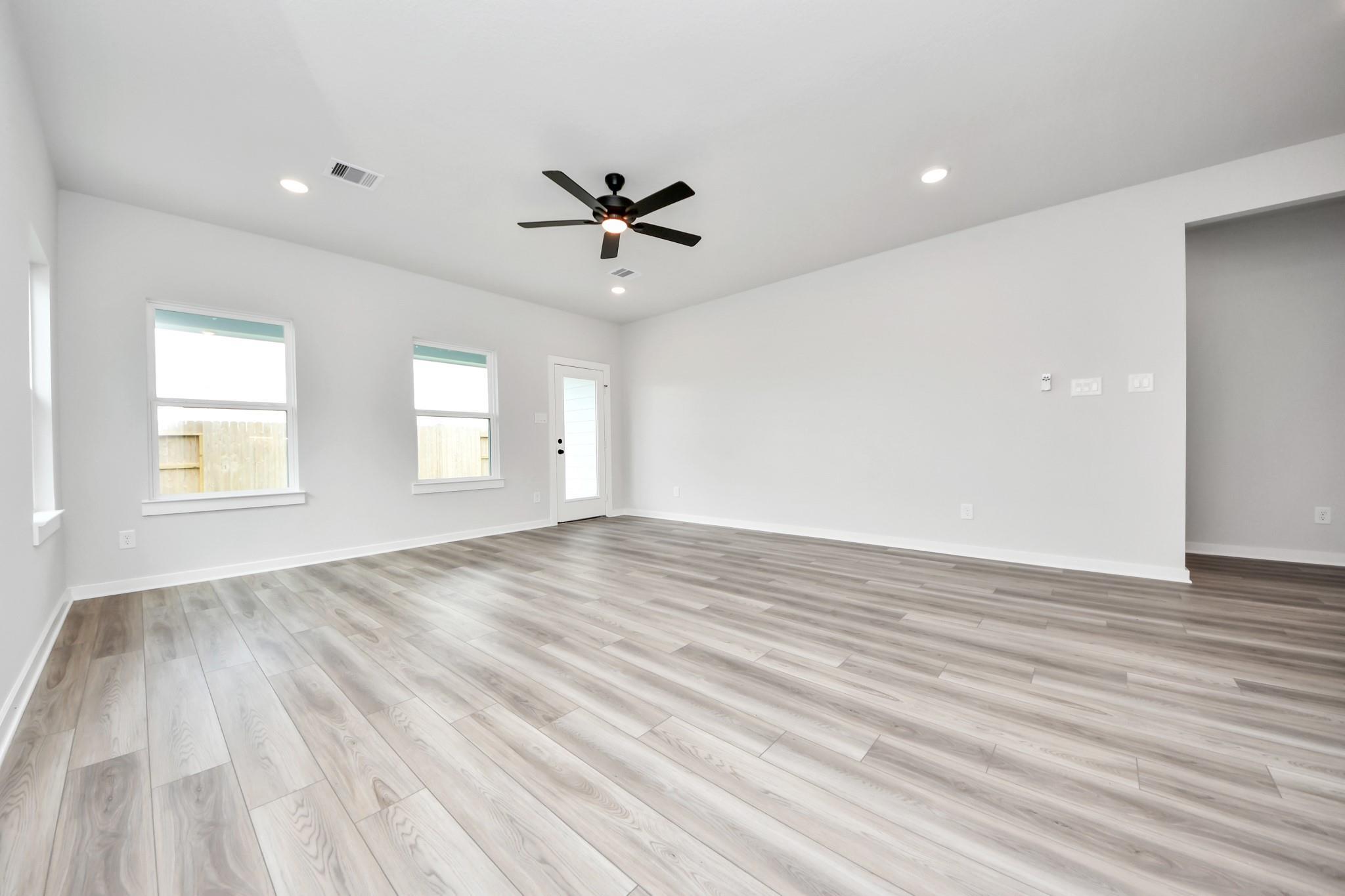 Spacious, light-filled living room with wood-look flooring in The Sorrento E floor plan by Davidson Homes in Crosby, Texas.