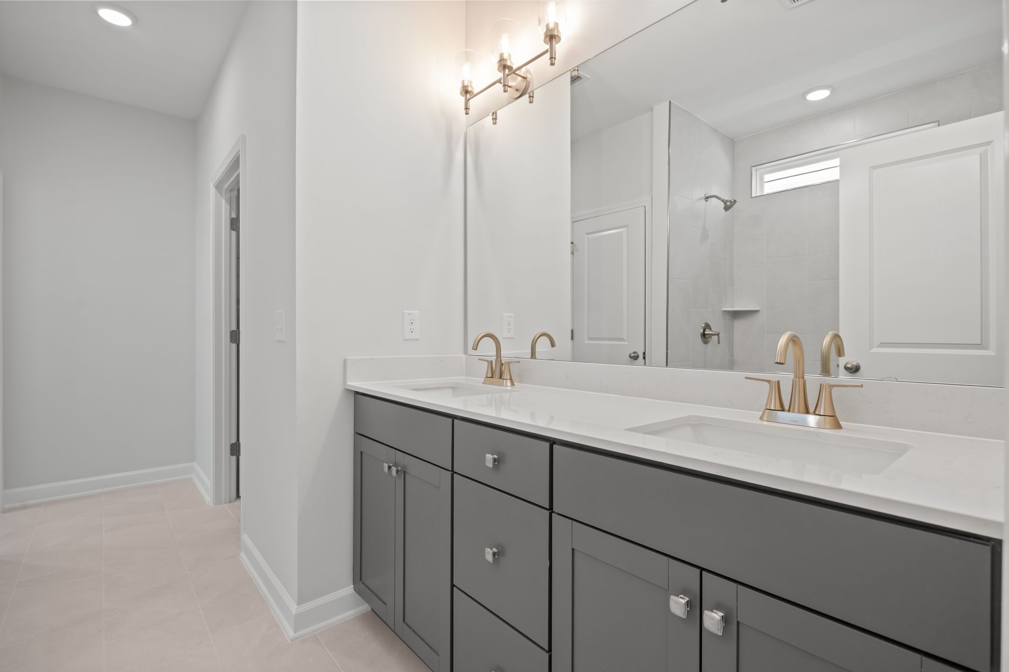 Primary bathroom in The Ashport B featuring a double vanity with grey cabinets, quartz countertops, and brass fixtures.