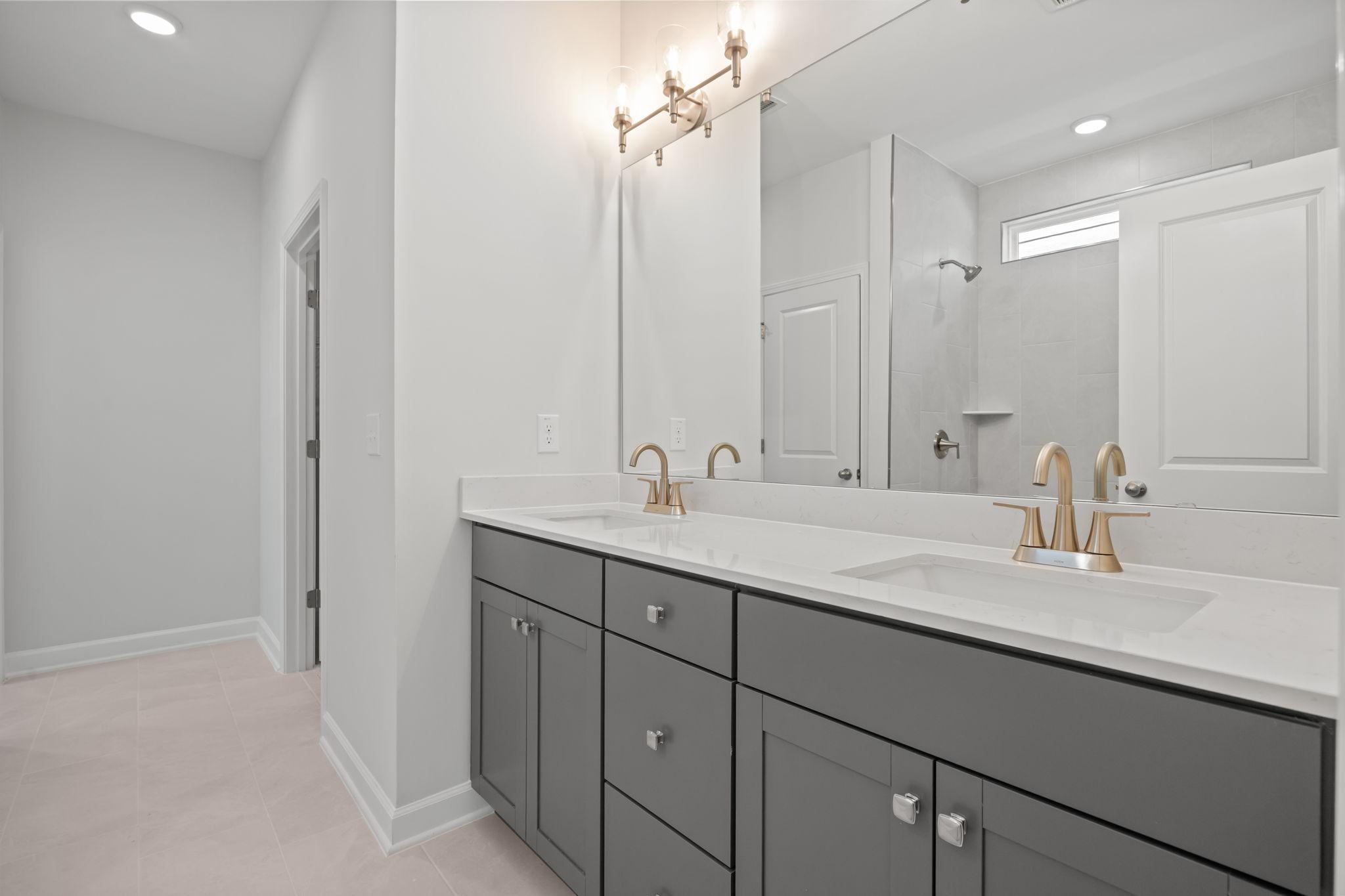 Primary bathroom in The Ashport B featuring a double vanity with grey cabinets, quartz countertops, and brass fixtures.