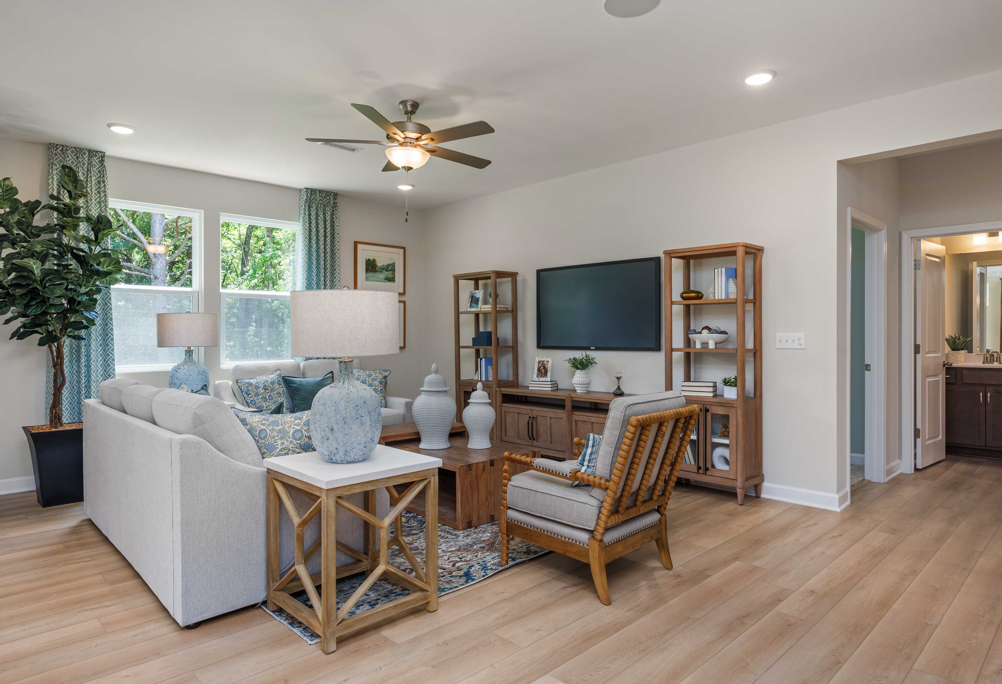 Spacious living room in The Willow G home design featuring white sectional sofa, wooden entertainment center with TV, potted plants, and hardwood floors