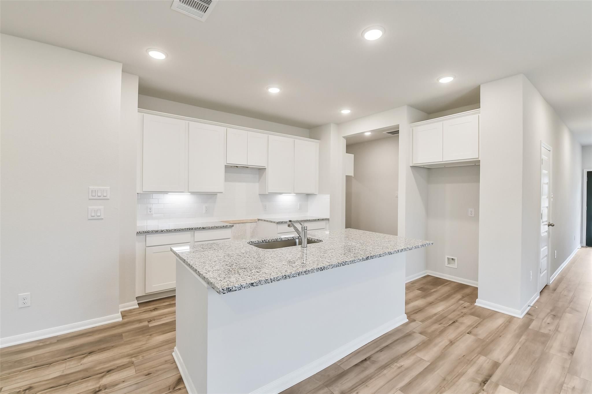 Modern white kitchen with granite island sink, stainless appliances, and hardwood floors in Davidson Homes The Brazos F, Conroe, TX