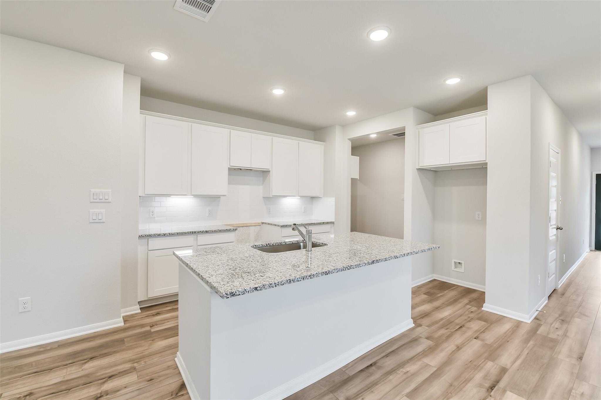 Modern white kitchen with granite island sink, stainless appliances, and hardwood floors in Davidson Homes The Brazos F, Conroe, TX