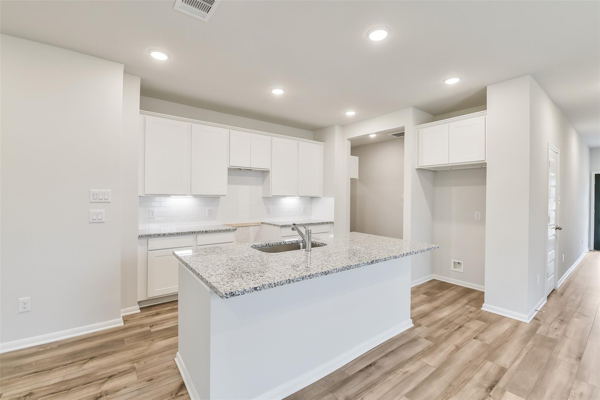 Modern white kitchen with granite island sink, stainless appliances, and hardwood floors in Davidson Homes The Brazos F, Conroe, TX