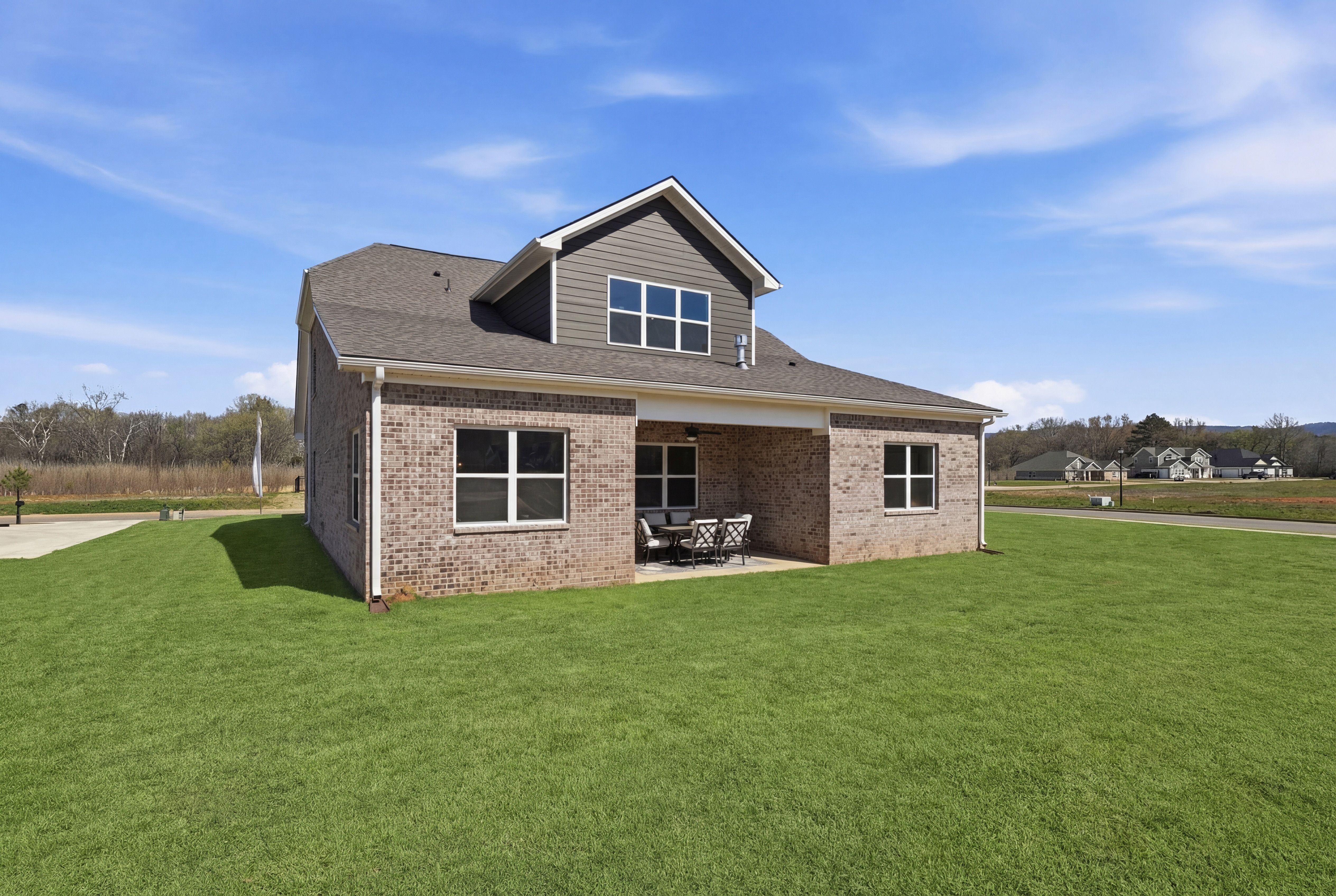 Contemporary brick home exterior with covered side porch and seating at The Meadows at Hampton Cove, Owens Cross Roads AL