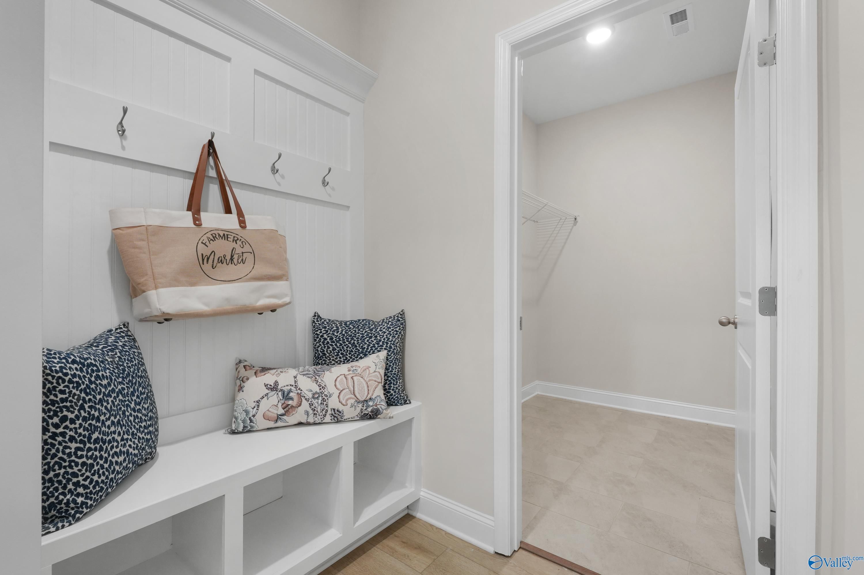 Cozy mudroom with white built-in bench, patterned pillows, coat hooks, and hanging tote in Davidson Homes The Rockford B, Toney, Alabama