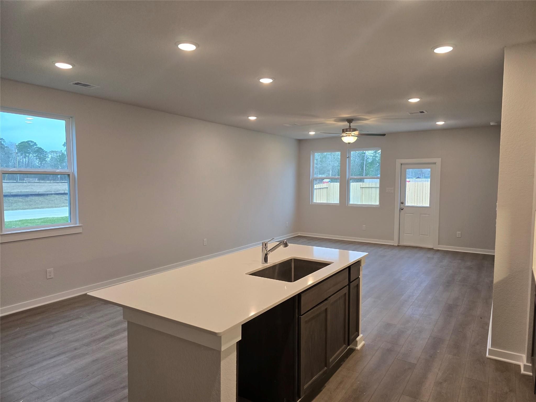 Modern open-concept kitchen with white quartz island, dark cabinets, hardwood floors, and backyard views in The Brazos E, Cleveland, Texas