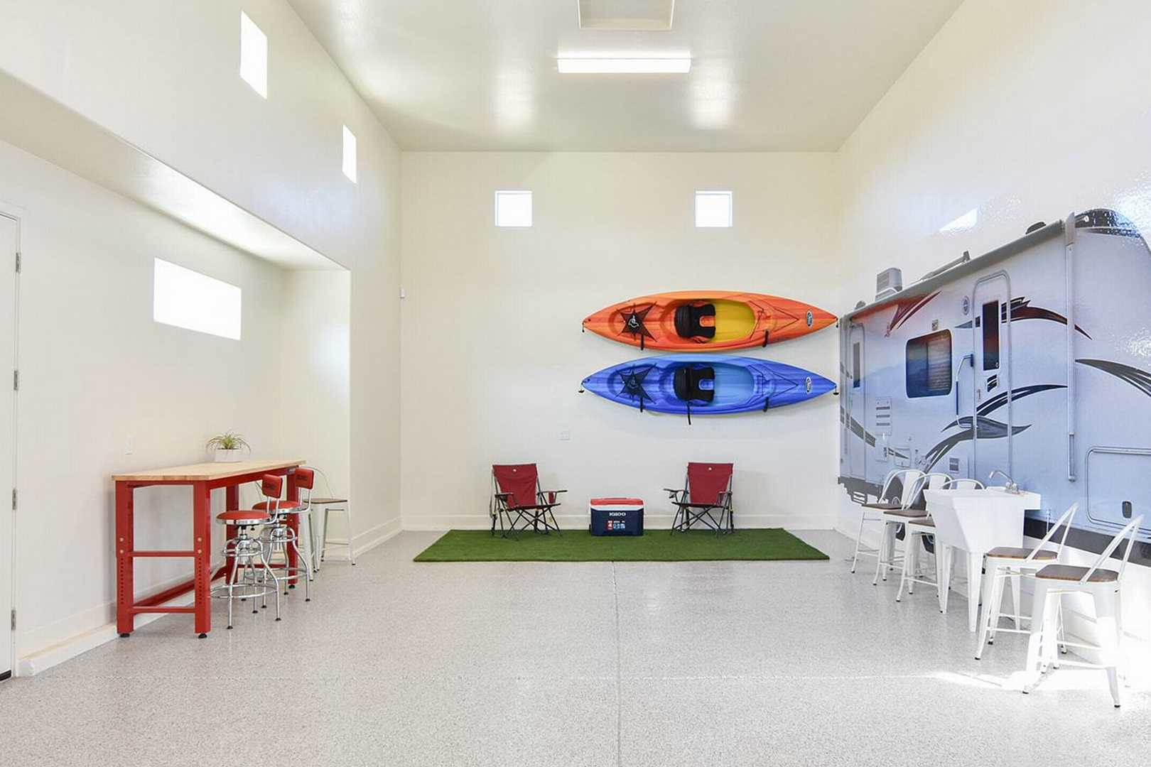 Spacious 3-car garage in The Summit B with RV wall mural, mounted red and blue kayaks, folding chairs, and turf area