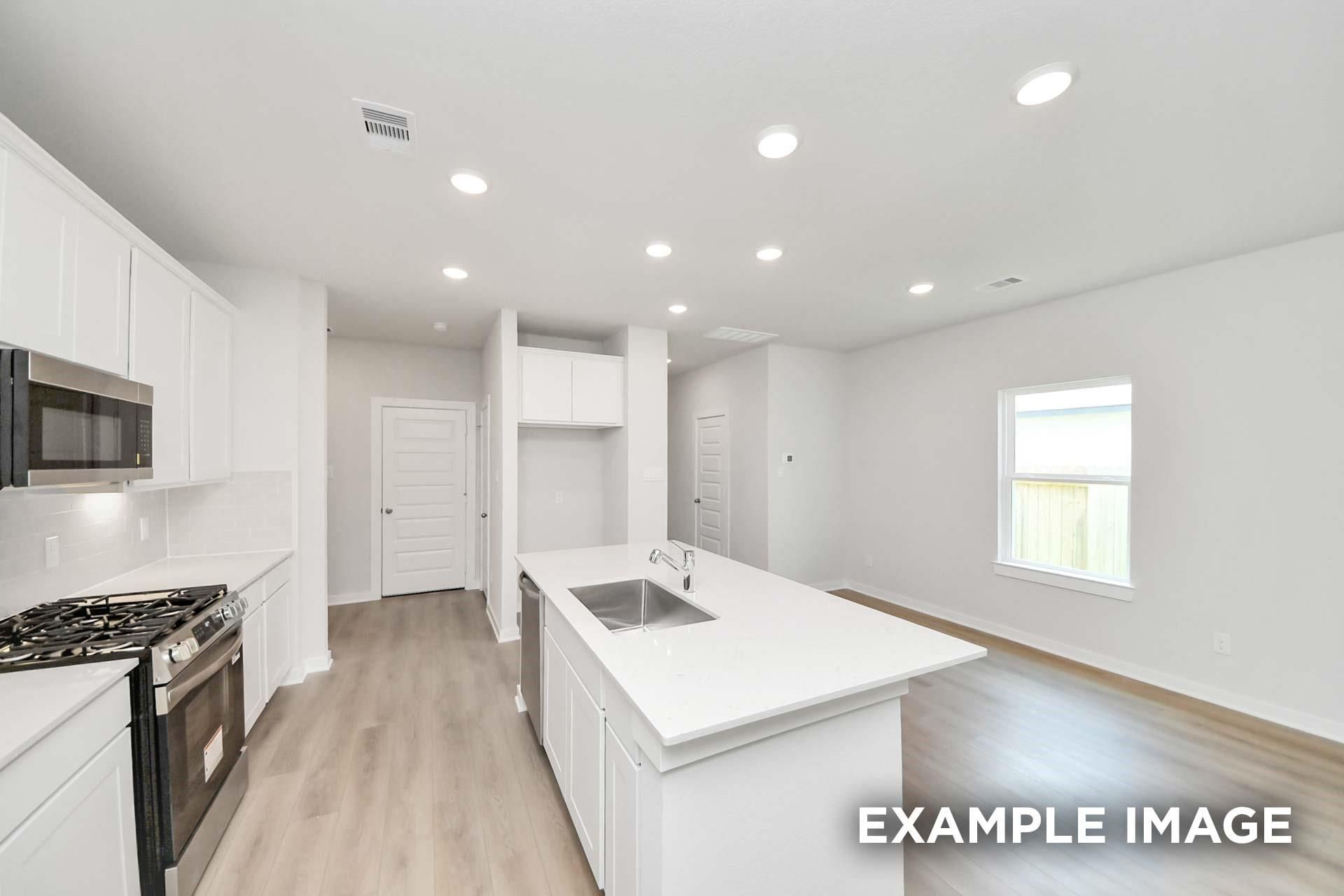 Open-concept kitchen with white shaker cabinets, quartz island, and stainless appliances in The Blanco E, Magnolia, Texas
