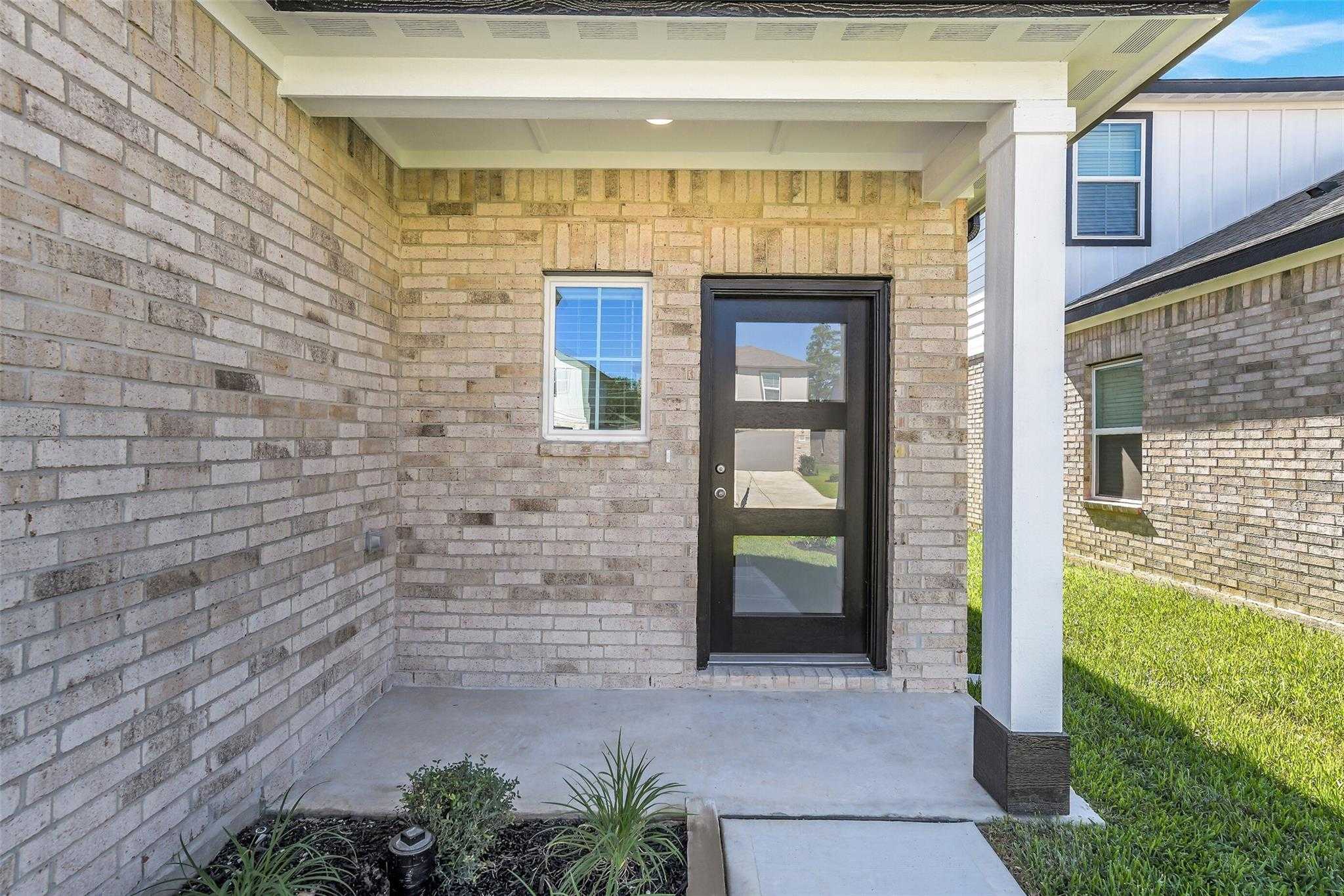 Contemporary brick home facade with black glass front door, porch plants, and garage in Davidson Homes The Rio Grande H, Magnolia, Texas