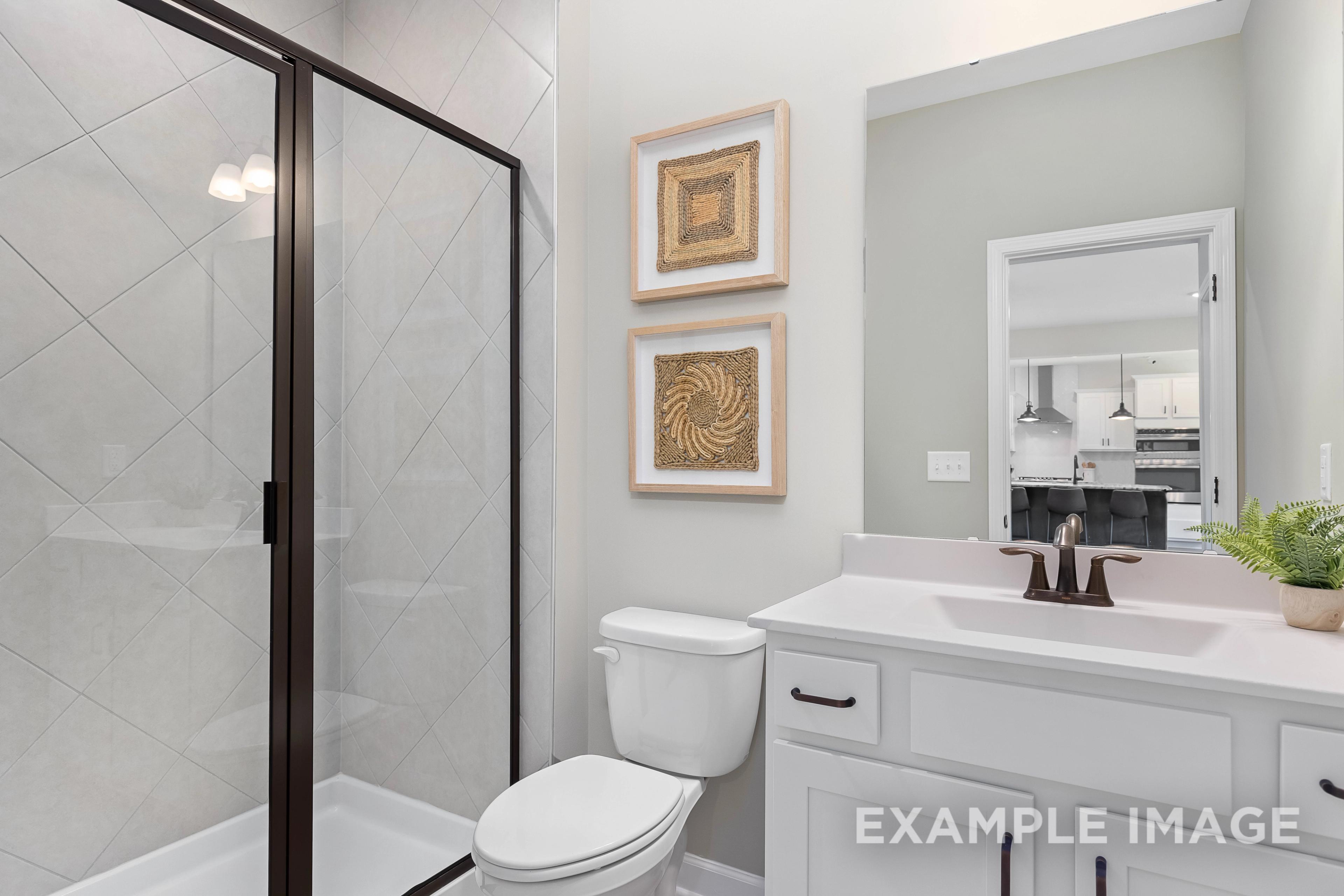 Spacious master bathroom in The Willow B featuring frameless glass shower, herringbone tile walls, white vanity, and woven art accents