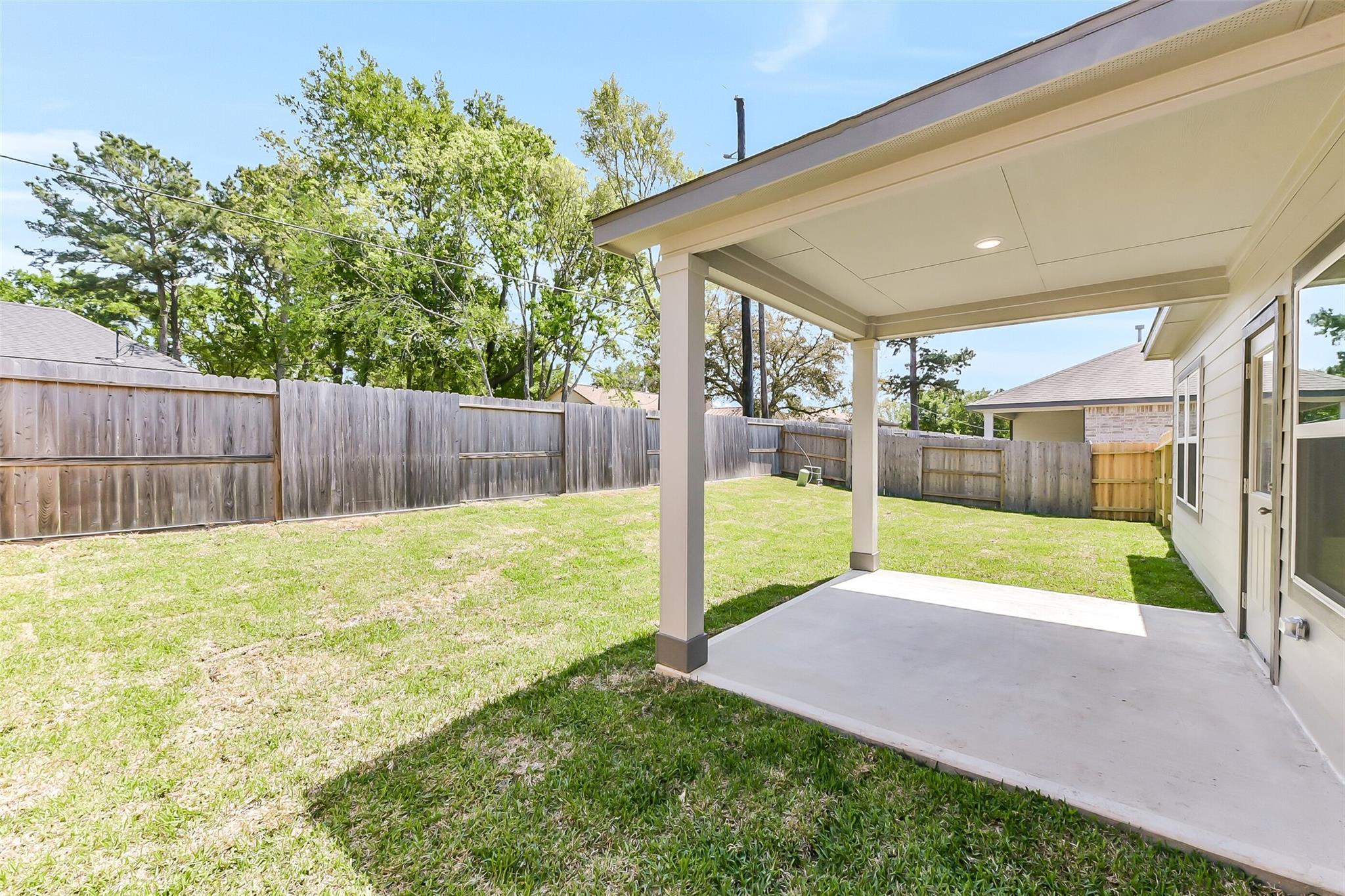Covered back patio with concrete slab overlooking fenced grassy yard in Davidson Homes The Brazos E, Windmill Estates, Magnolia, Texas
