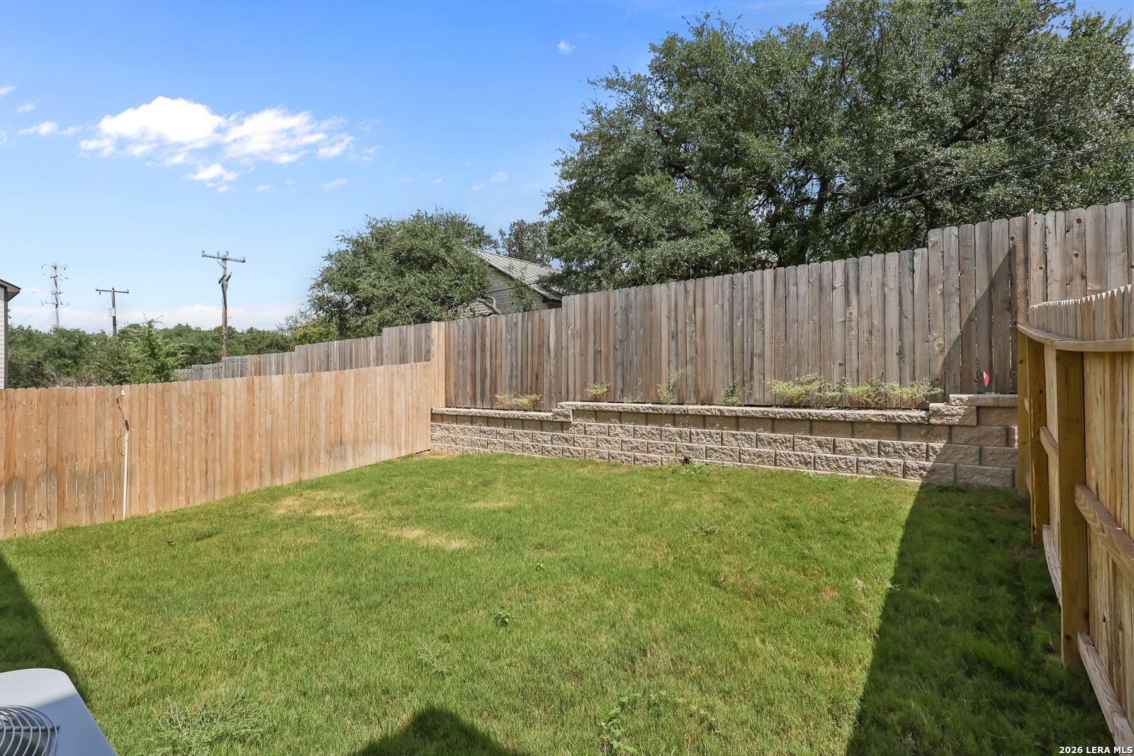 Private backyard with wood privacy fence and tiered retaining wall in Meadows at Oak Creek, San Antonio, Texas.