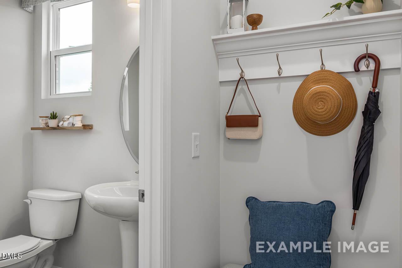 Bright powder room with white pedestal sink, toilet, mirror, and coat hooks holding hat and umbrella in Davidson Homes The Graham, Fuquay-Varina, NC