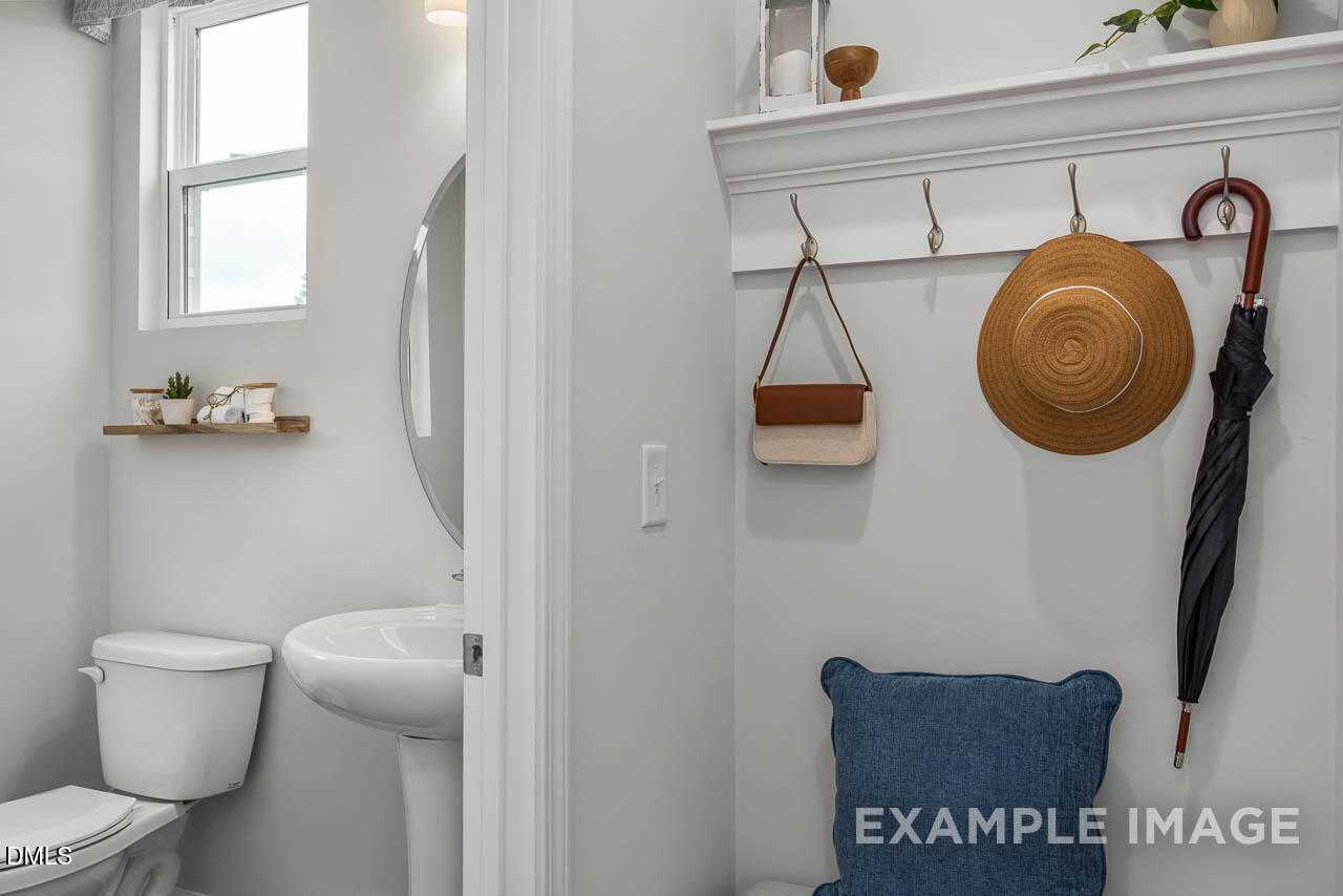 Modern powder room with white sink, toilet, and wall hooks holding hat, umbrella, bag in Davidson Homes The Graham, Fuquay-Varina, NC