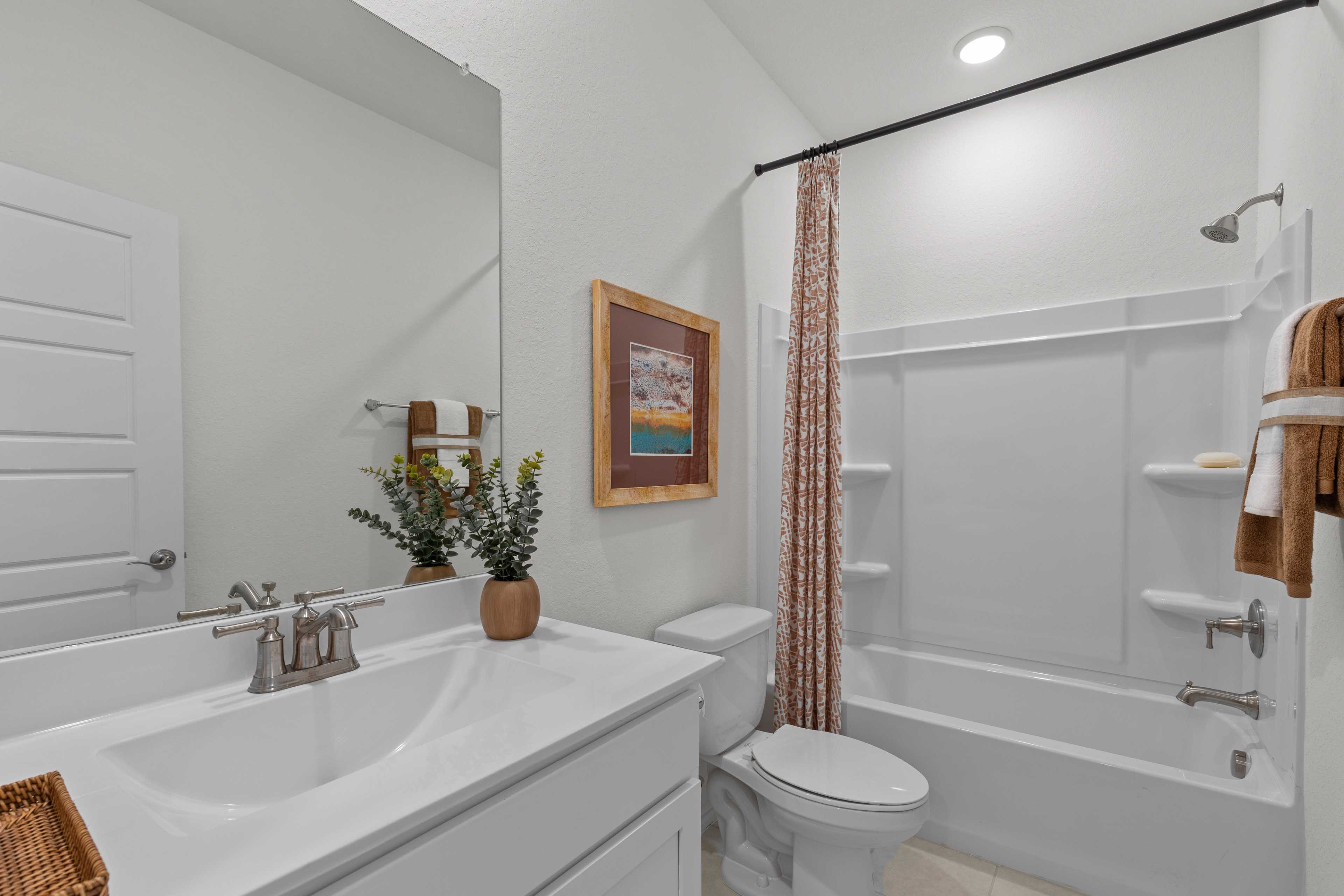 Spacious master bathroom in The Daphne H with white subway tile tub, double sink vanity, potted plant, and framed art