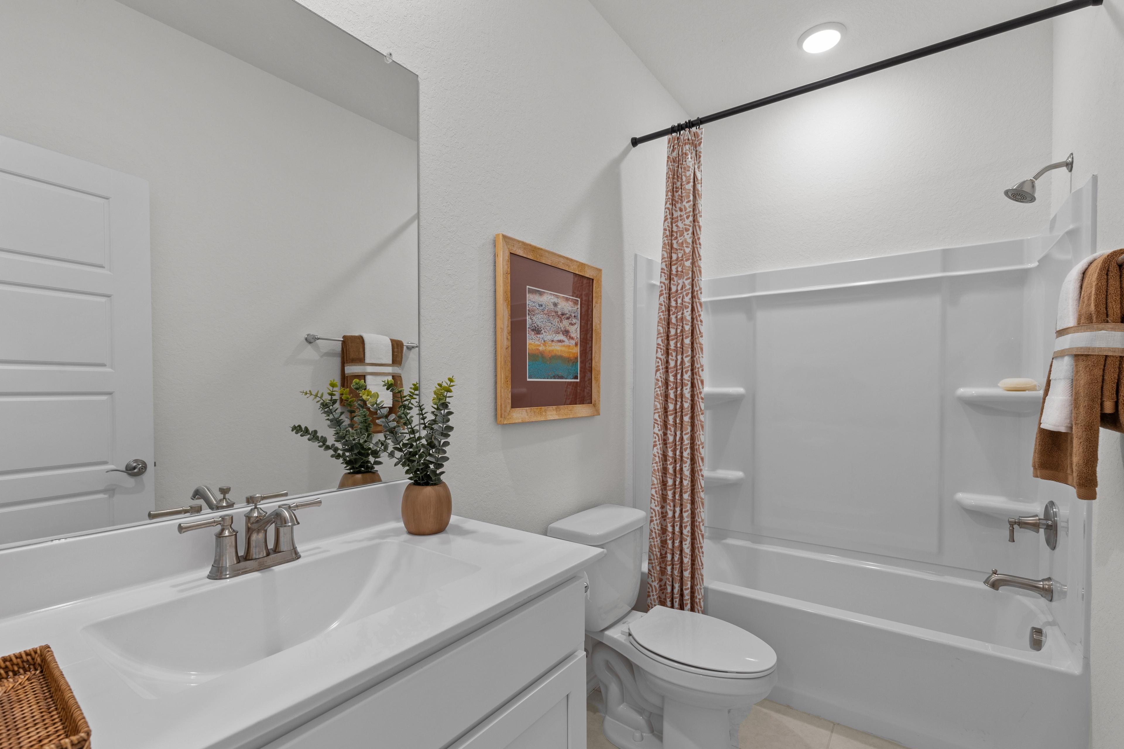 Spacious master bathroom in The Daphne G with white vanity, tub shower, potted plant, and framed art accents