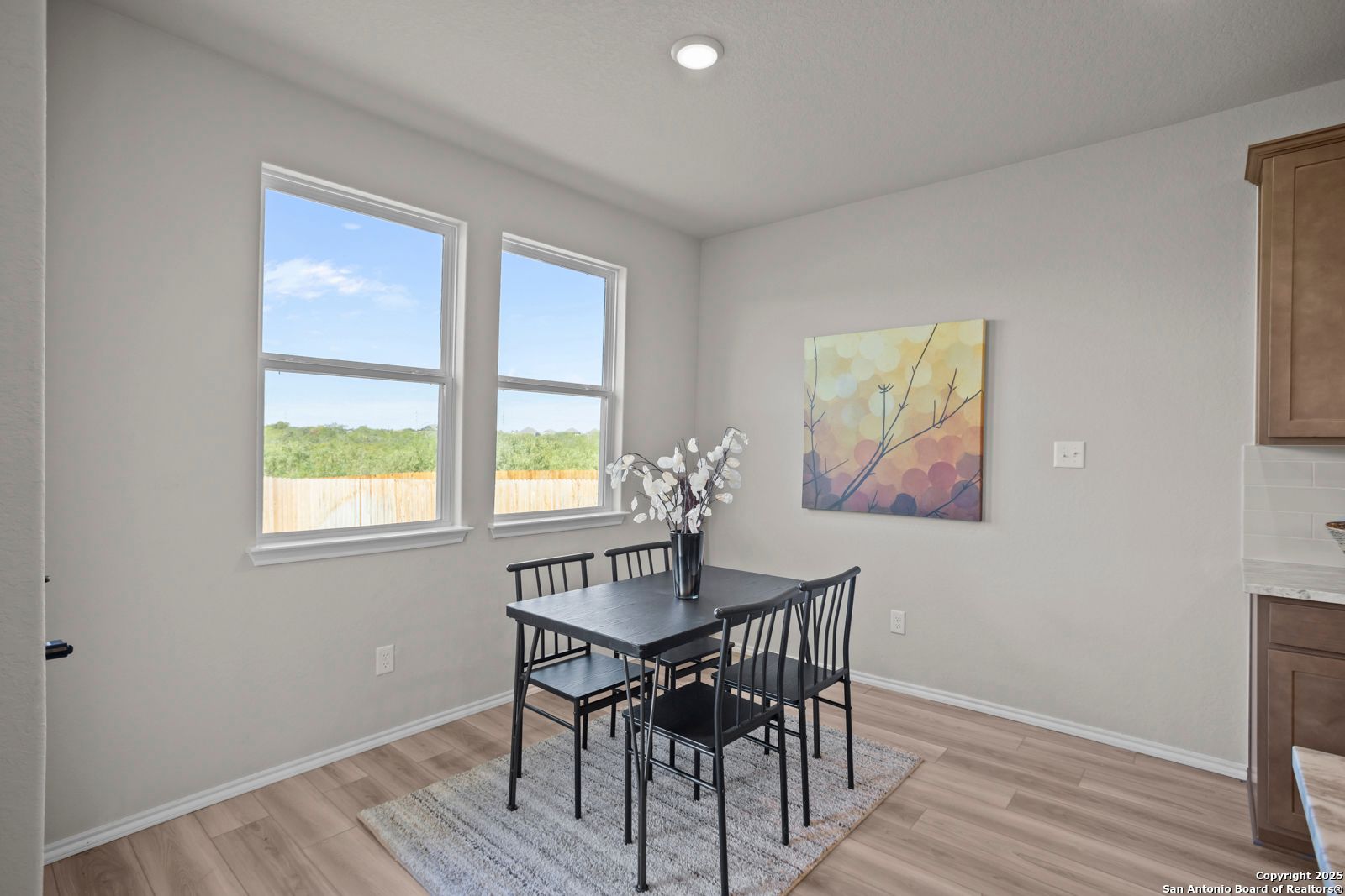 Cozy dining nook with black table, chairs, white floral vase, abstract yellow art, and backyard views through large windows in The Asheville H, Converse, Texas