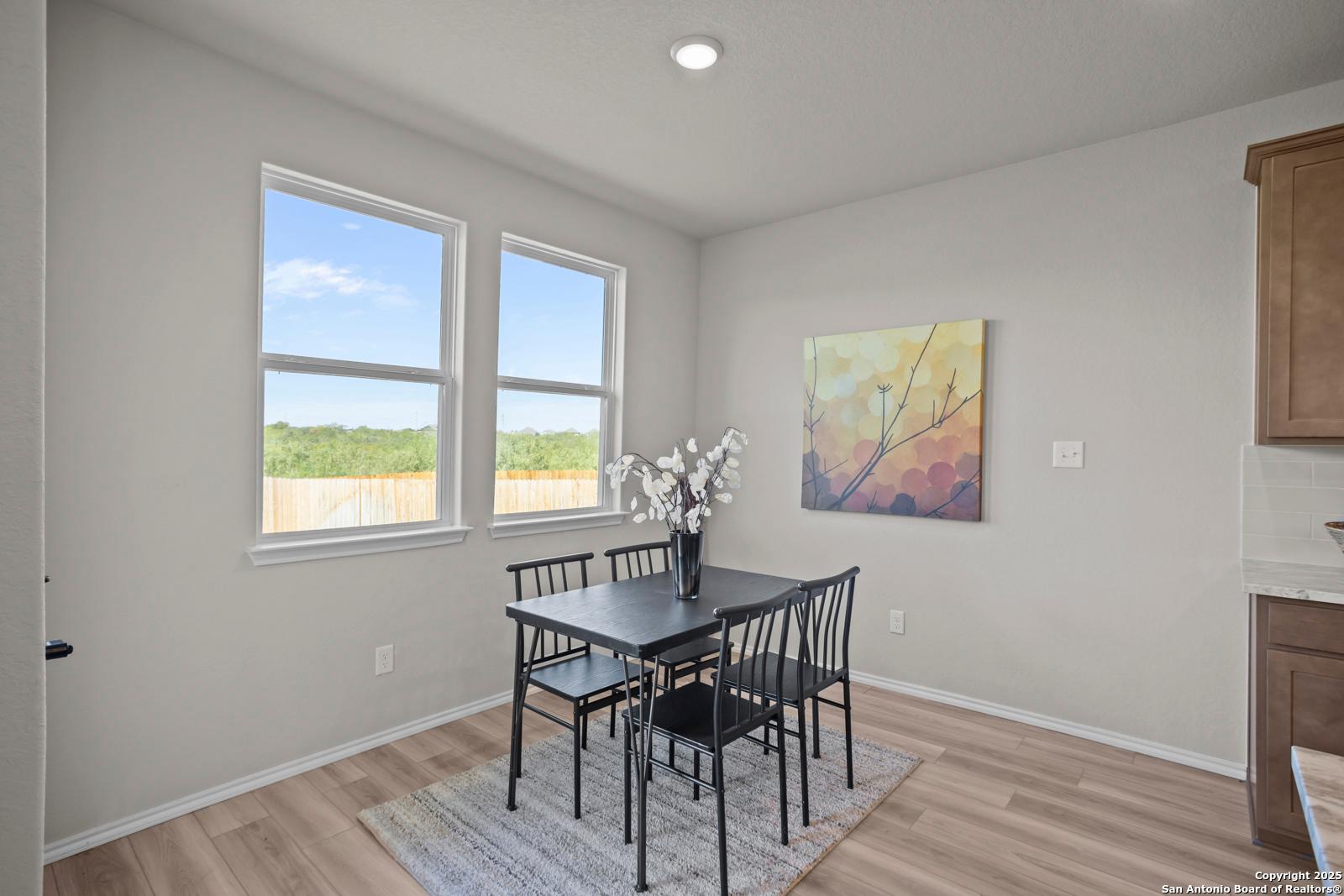 Cozy dining nook with black table, chairs, white floral vase, abstract yellow art, and backyard views through large windows in The Asheville H, Converse, Texas