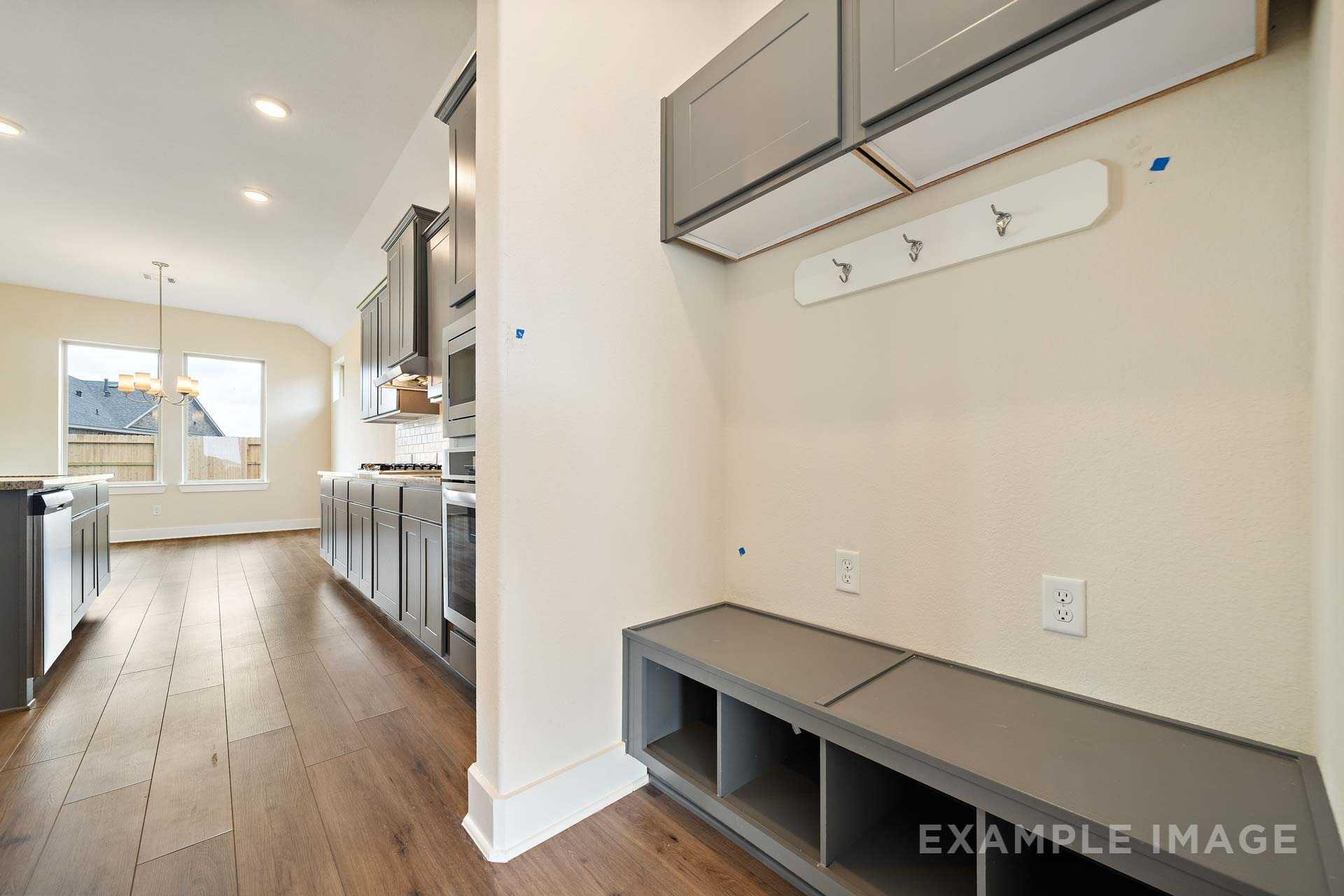 Spacious mudroom in The Diana C home design with built-in gray bench, cubbies, coat hooks, and adjacent modern kitchen