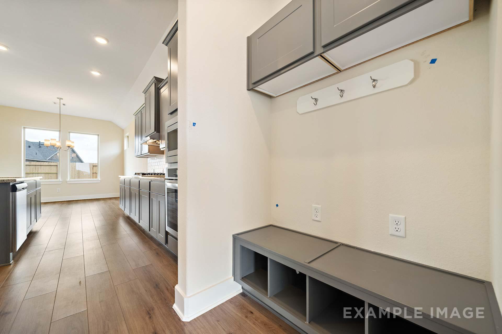 Spacious mudroom in The Diana C home design with built-in gray bench, cubbies, coat hooks, and adjacent modern kitchen