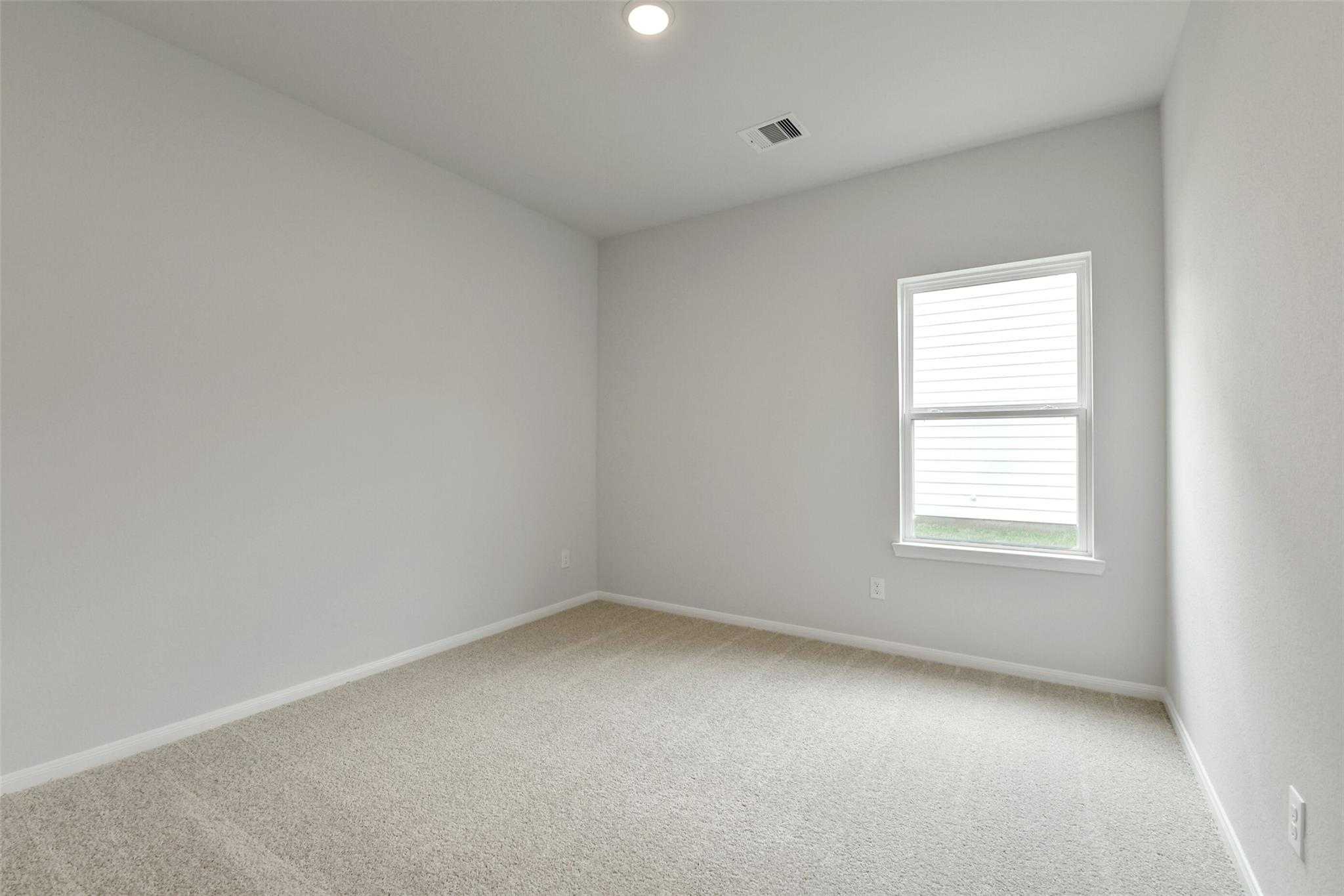 Empty secondary bedroom with light gray walls, beige carpet, and large window in Davidson Homes The Frio G, Conroe, Texas