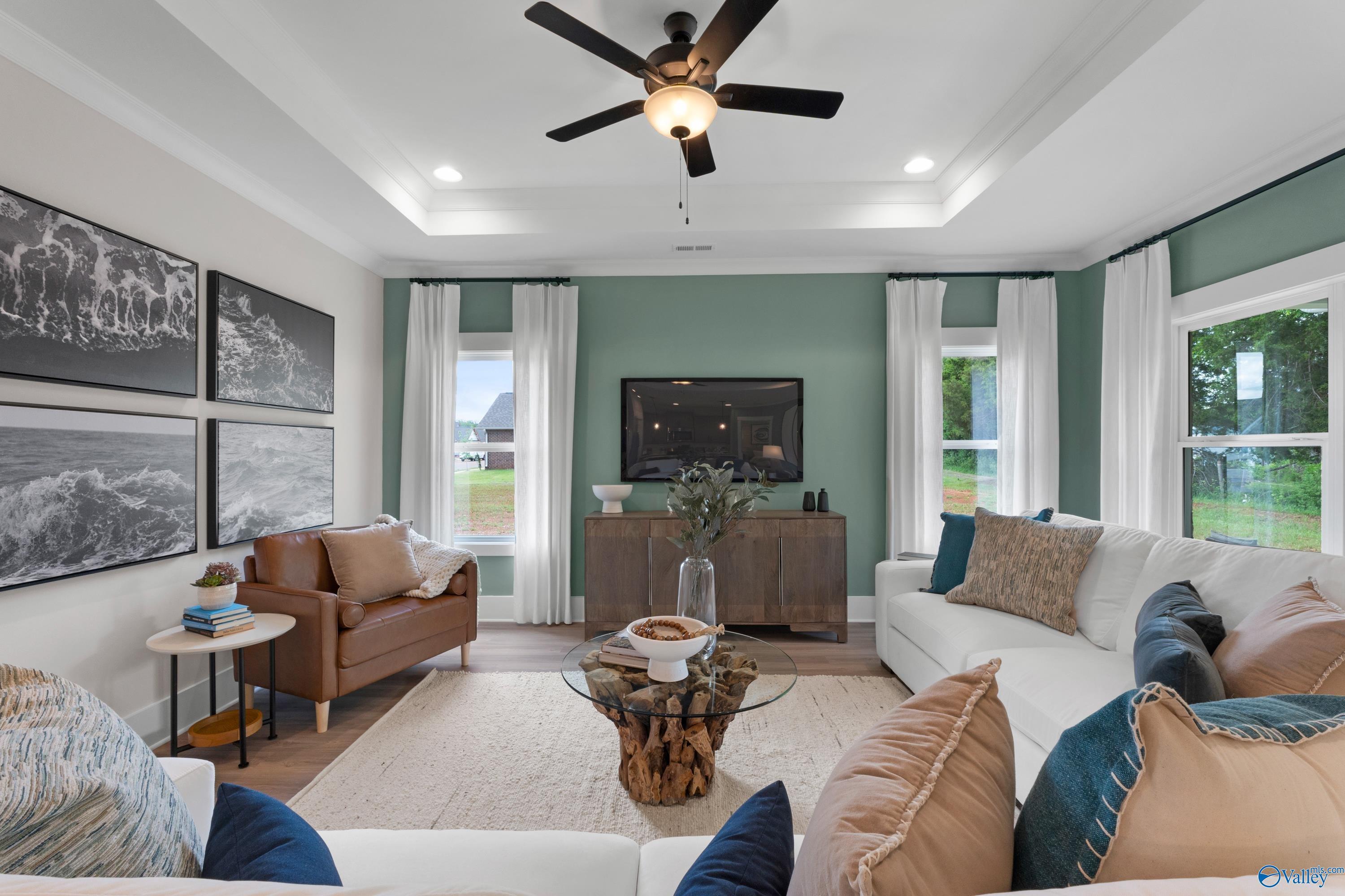 Modern living room with tray ceiling, green accent wall, and cozy seating in The Franklin floor plan, Hollon Meadow.