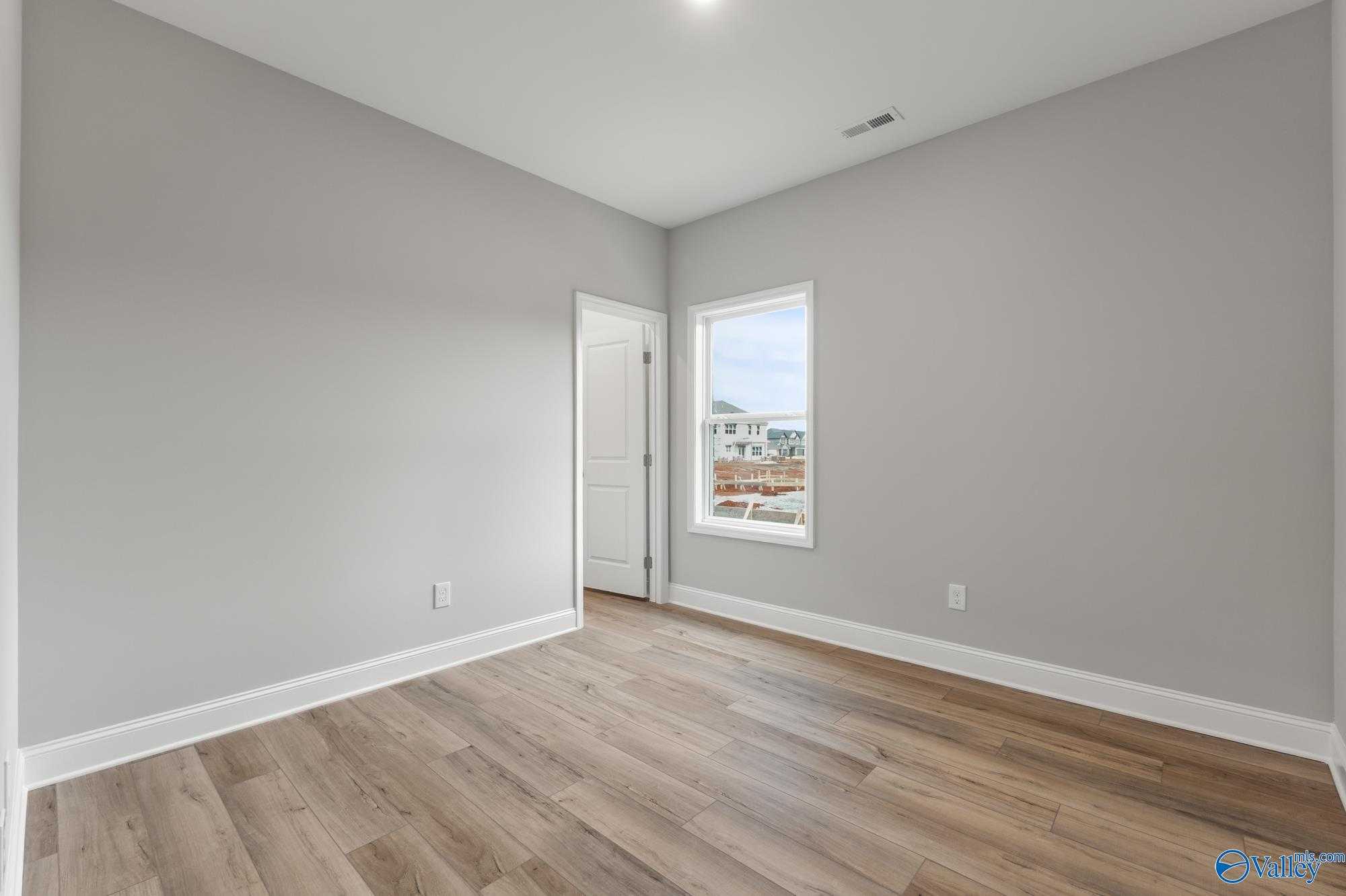 Bright bedroom corner with gray walls, hardwood floors, interior door, and window view in Davidson Homes The Daphne D, Athens AL