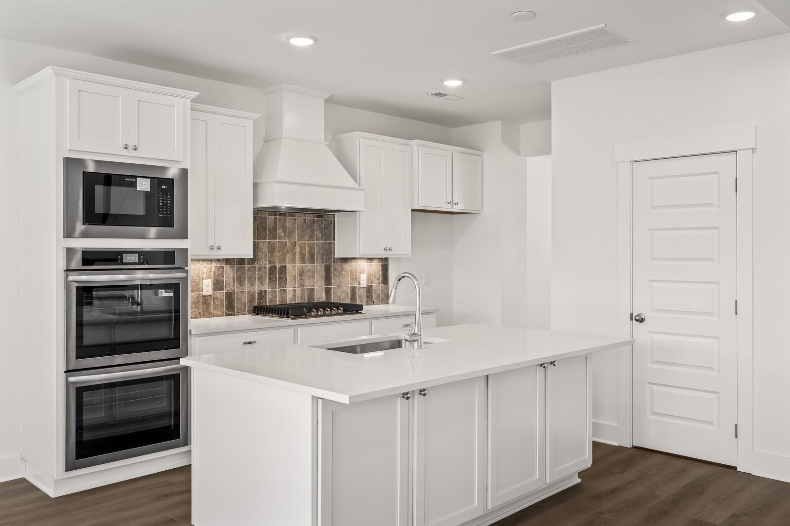 Modern white kitchen with stainless steel double oven, island sink, shiplap backsplash in Davidson Homes The Willow D, Mt. Juliet