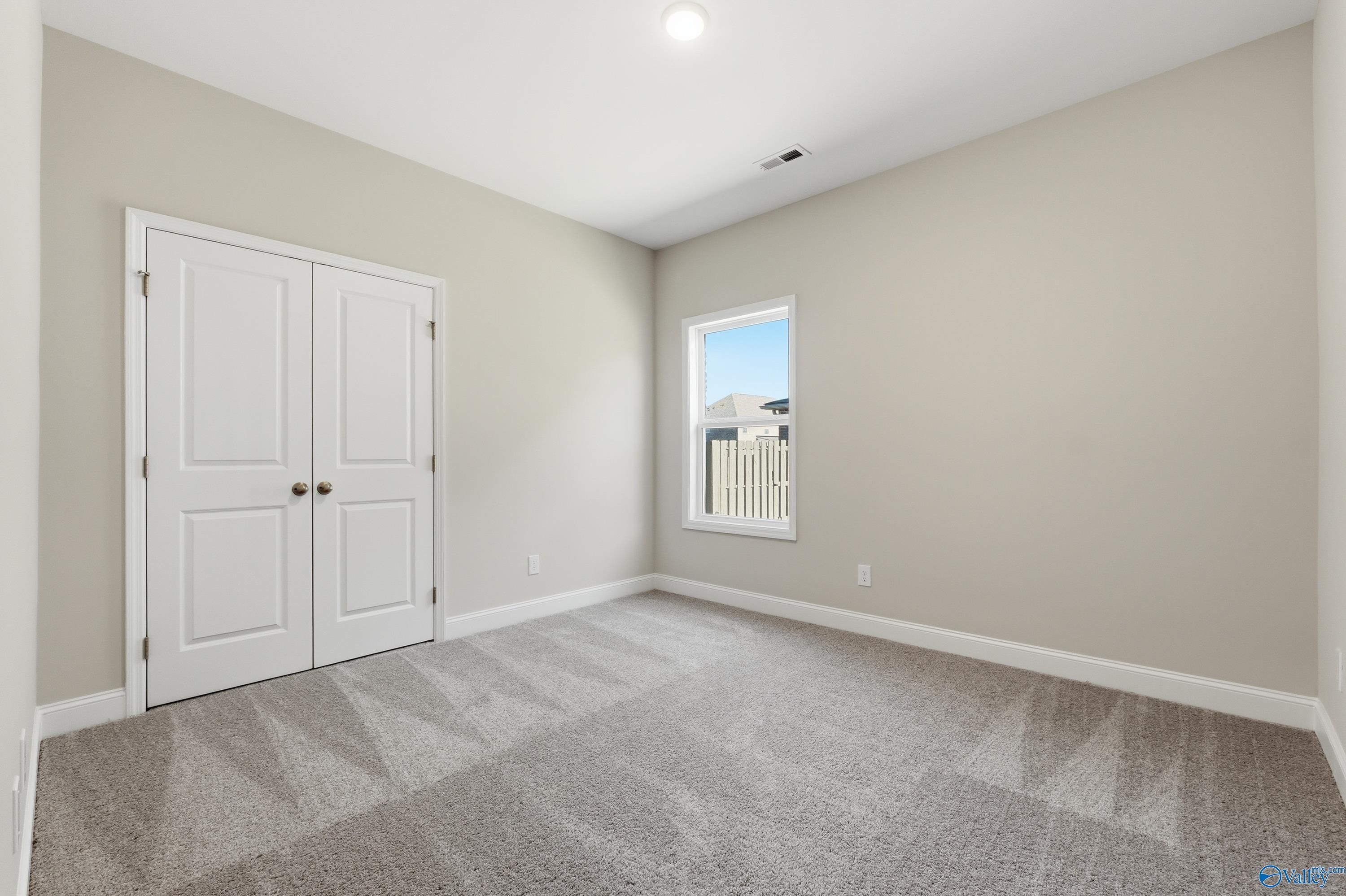 Cozy secondary bedroom featuring beige walls, white double doors, window blinds, and neutral carpet in Davidson Homes The Everett, Harvest, Alabama