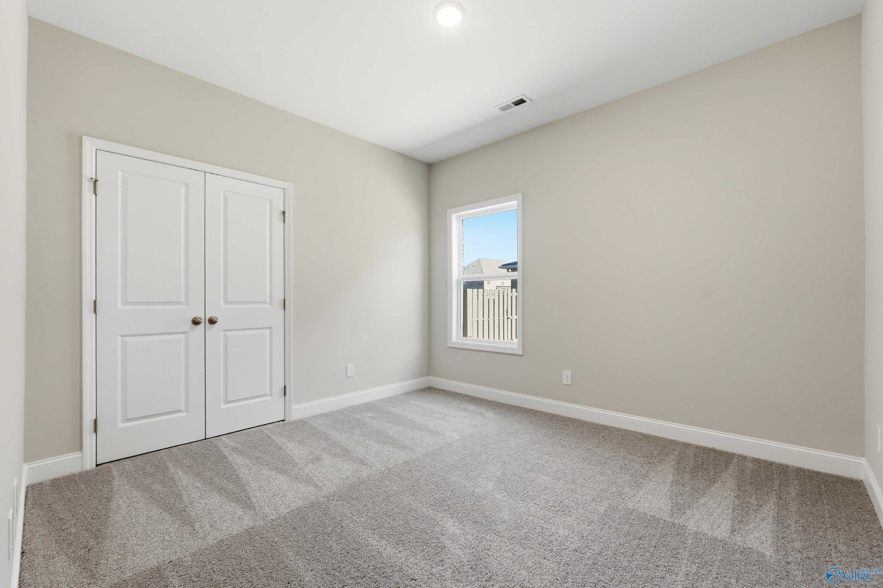 Cozy secondary bedroom featuring beige walls, white double doors, window blinds, and neutral carpet in Davidson Homes The Everett, Harvest, Alabama
