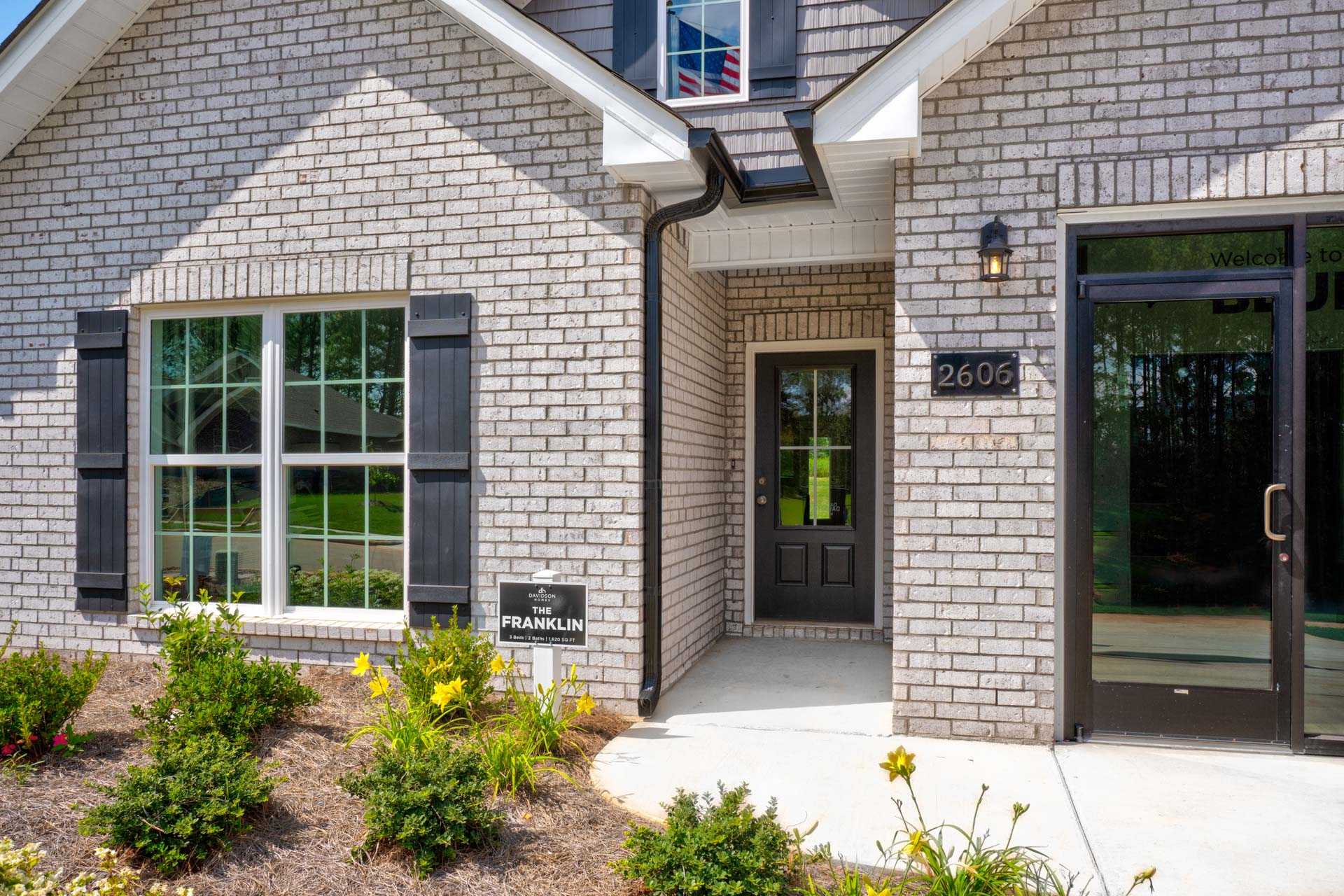 Brick home exterior at Blue Spring in Huntsville AL with gray facade, shutters, covered porch, and landscaped plants