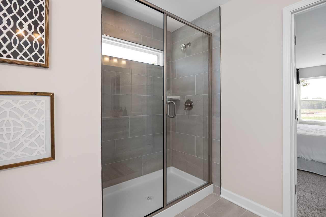 Frameless glass shower in master bath at Wellers Knoll Lillington NC with gray subway tiles rainfall showerhead and decorative wall art