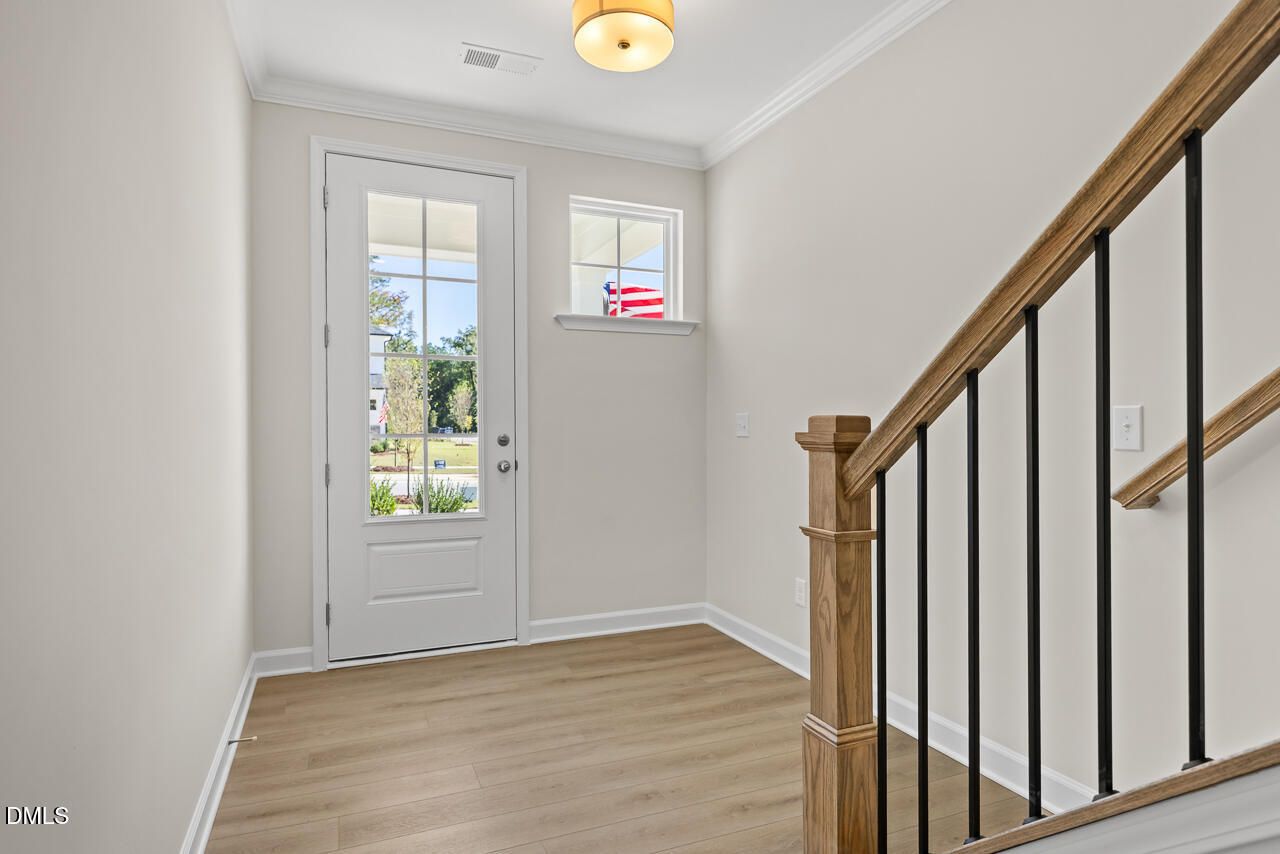 Bright foyer with glass-panel front door, hardwood floors, and oak staircase in Davidson Homes The Preston B, Wendell Ridge, NC